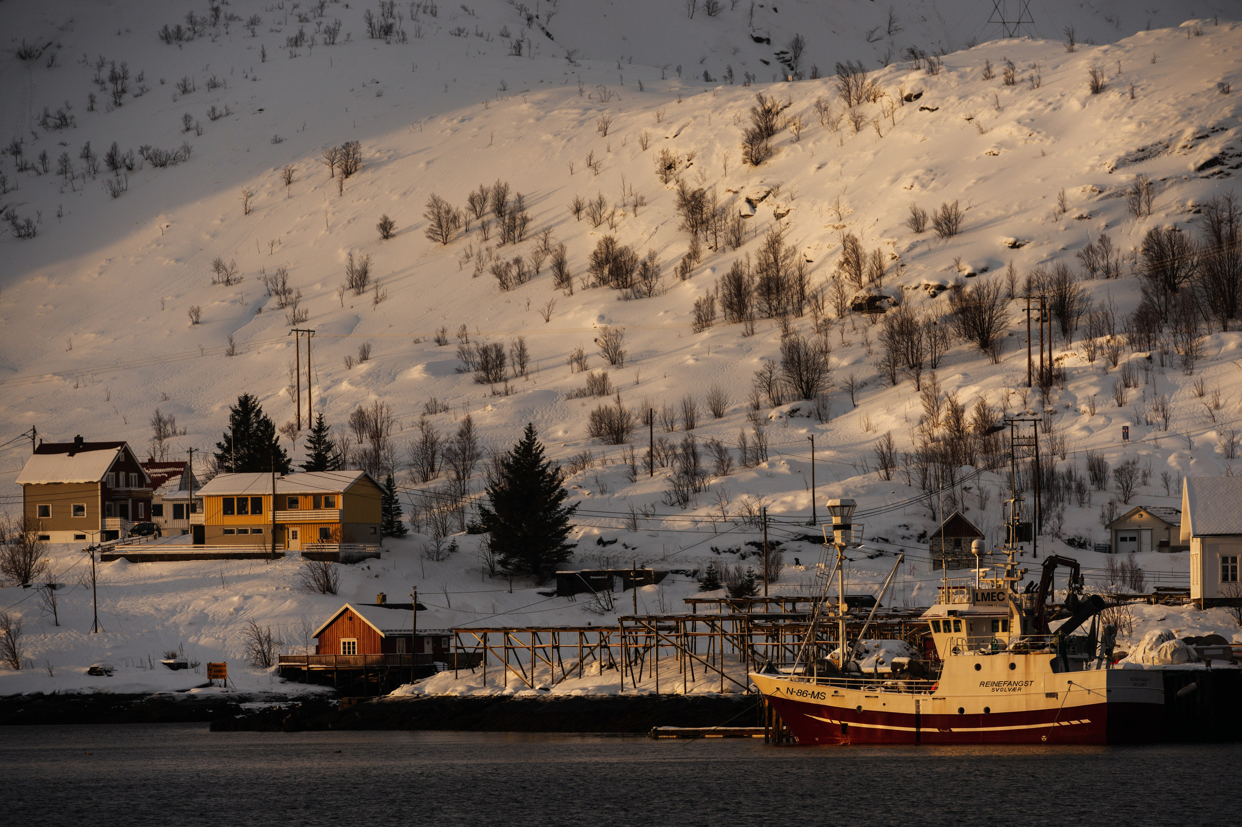 Рыболовецкое судно пришвартовано в заснеженной гавани норвежской деревни на Лофотенских островах.