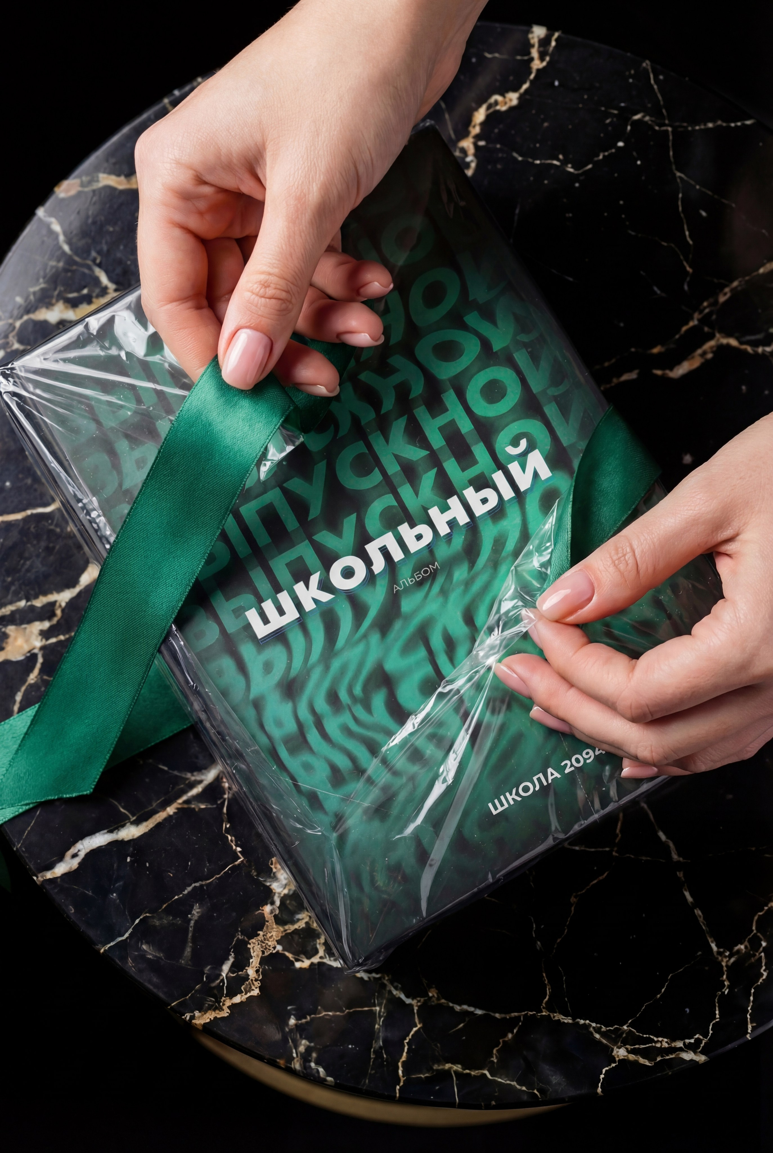 Руки упаковывают зелёный фотоальбом в прозрачную плёнку