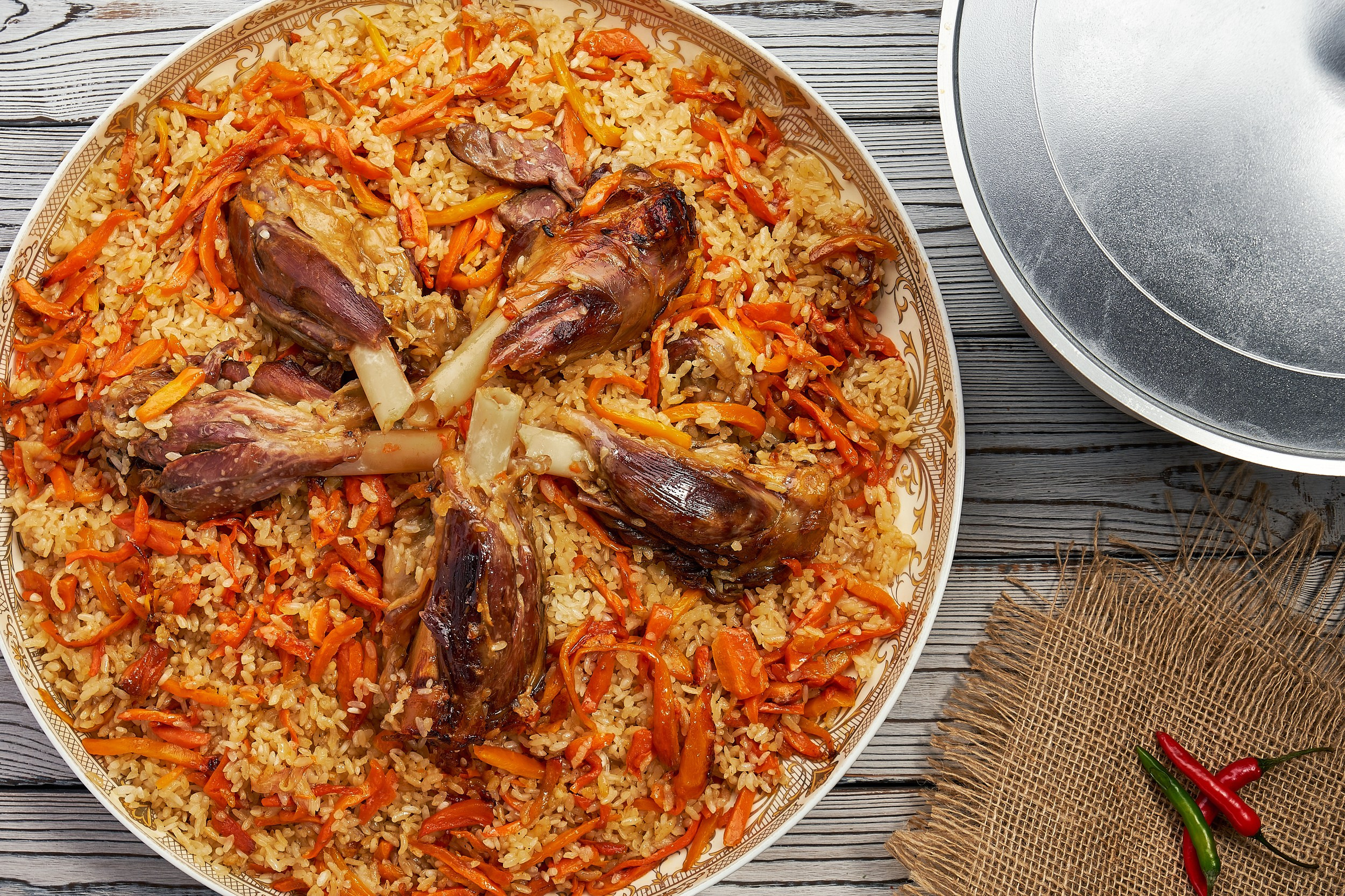 Плов с бараниной, морковью и рисом, поданный в традиционной восточной тарелке. Сочное мясо на кости, рассыпчатый рис и яркая подача — классика кухни в казане