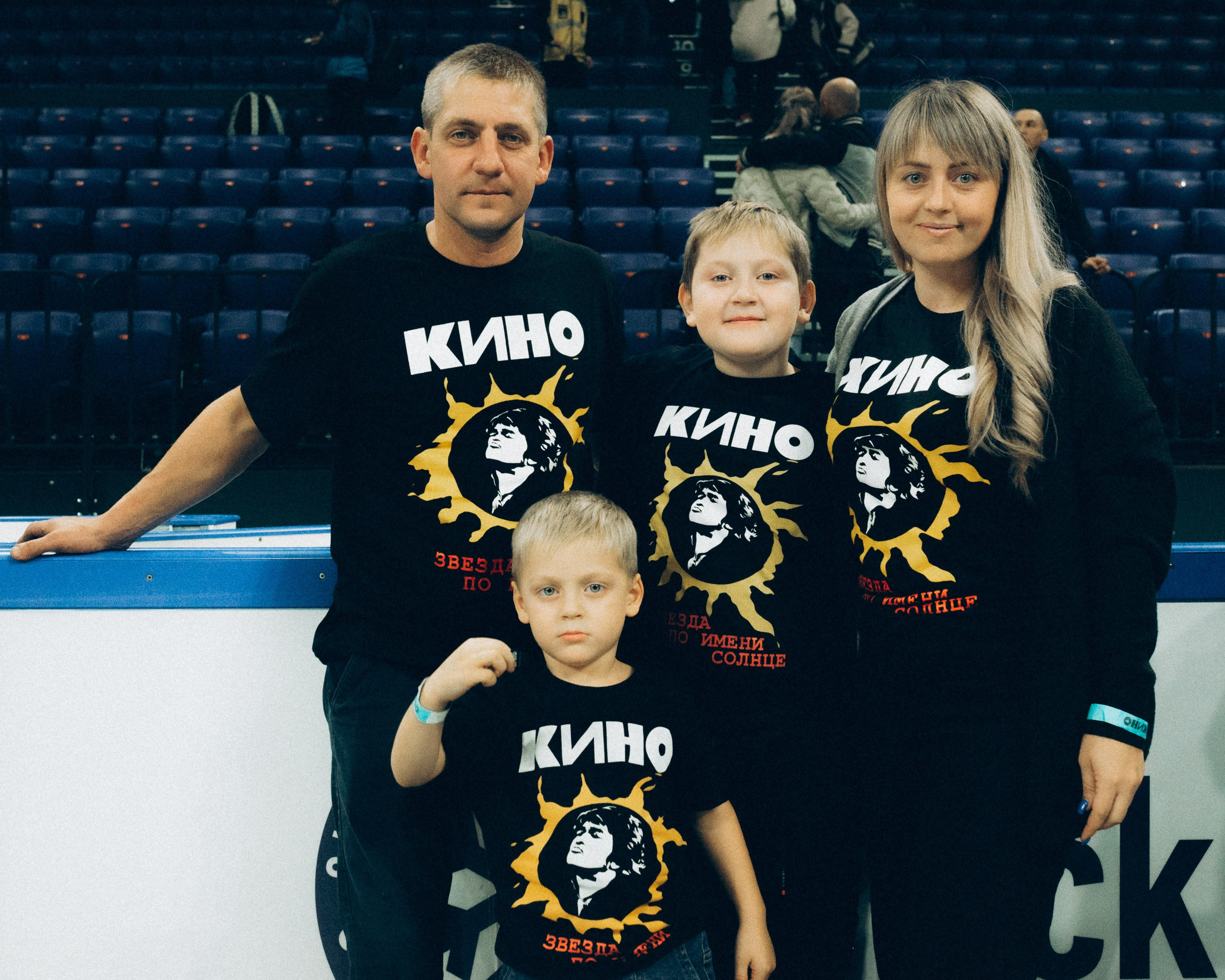 Семейное фото на концерте КИНО: родители и дети в одинаковых футболках "Звезда по имени Солнце" на фоне трибун Сибирь-Арены