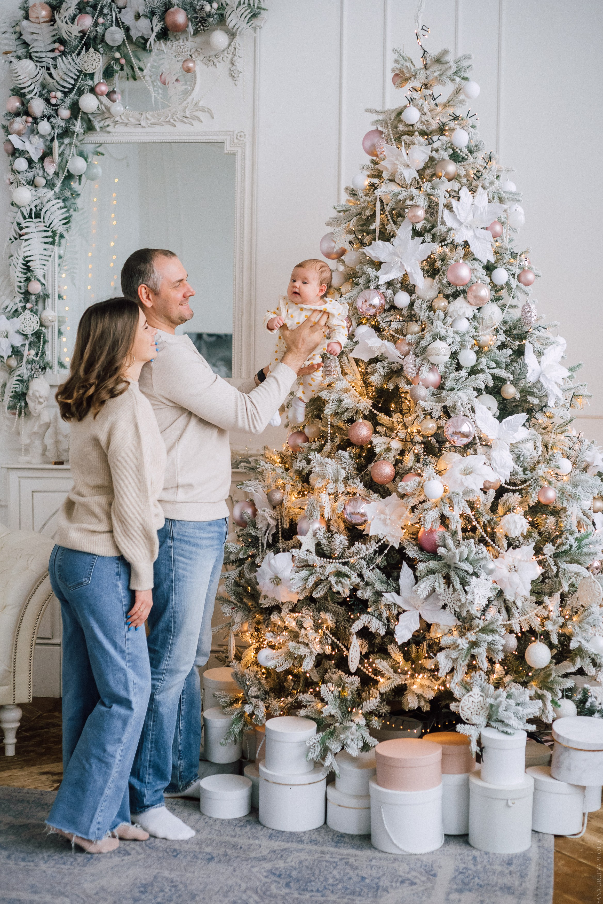 Папа и мама держат младенца на фоне новогодних декораций