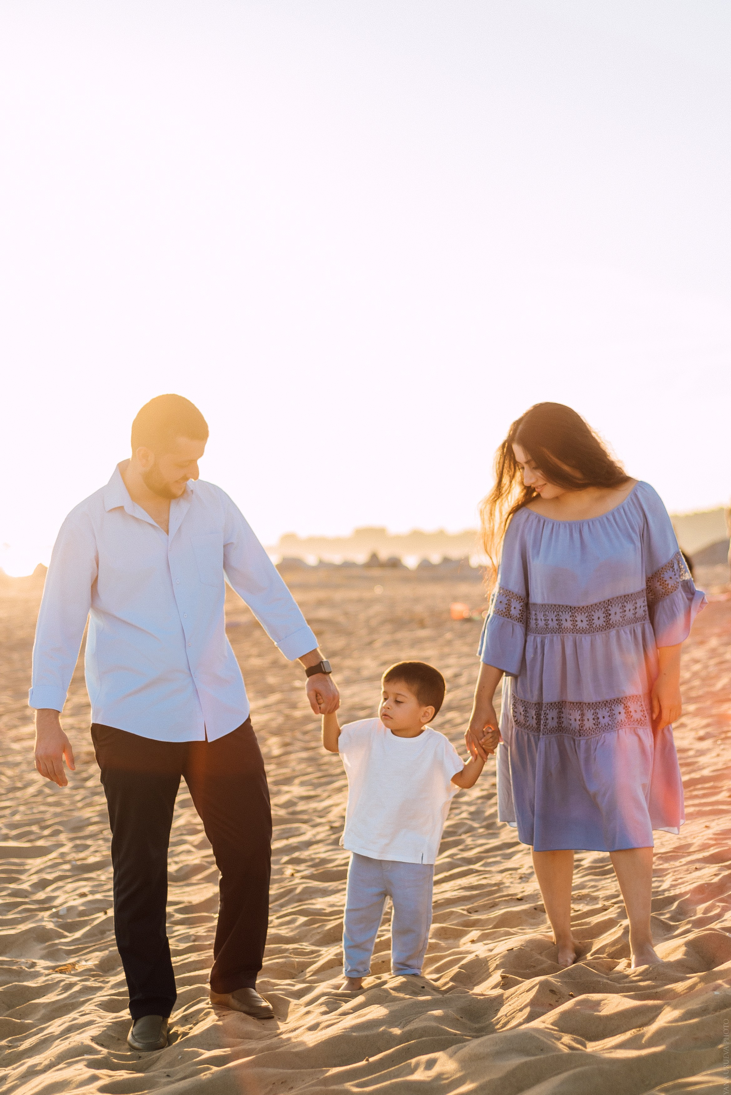 Сын держит за руки маму и папу , они идут по пляжу