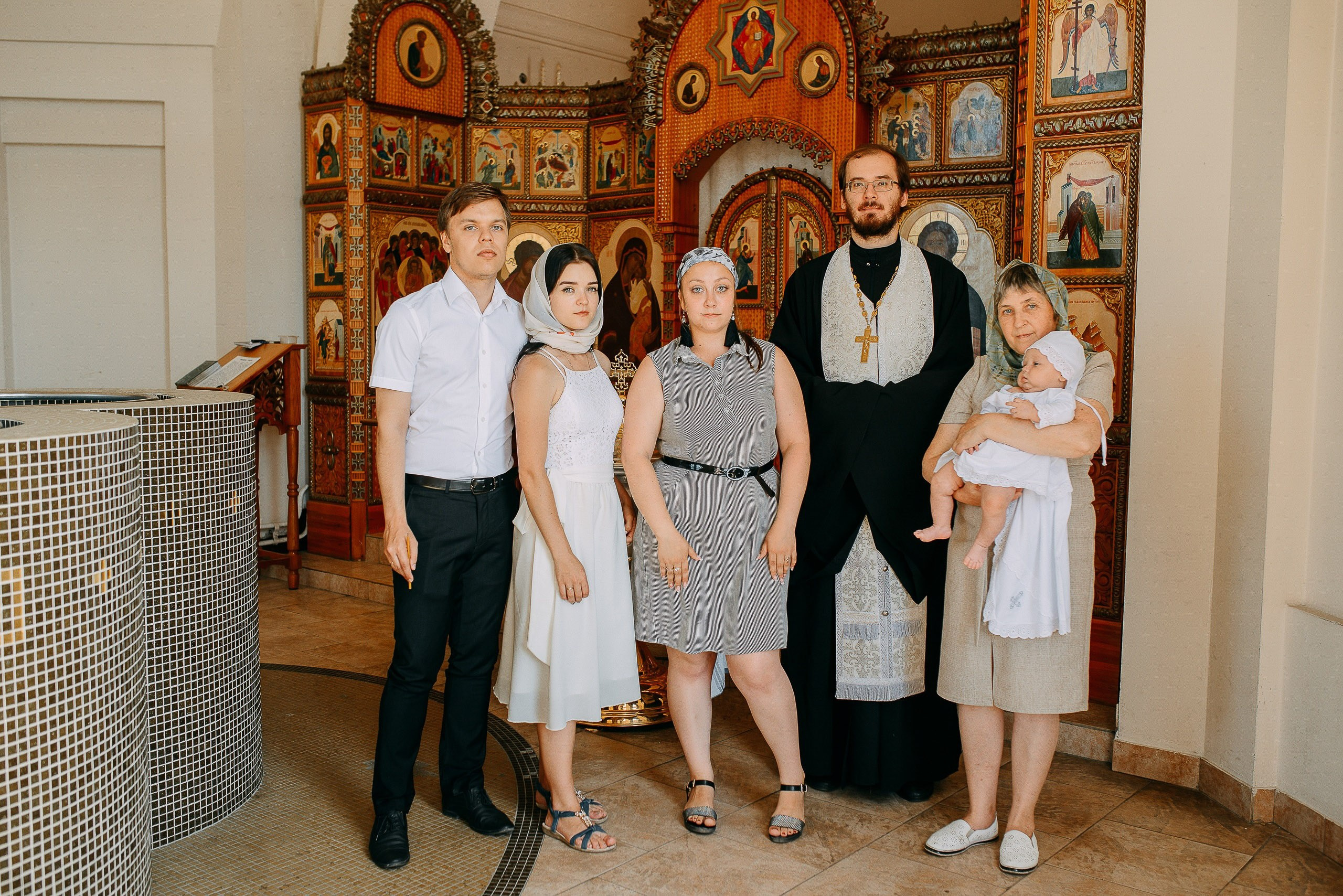 Семейное фото после крещения в храме Новосибирска с родителями, крестными и священником на фоне иконостаса.
