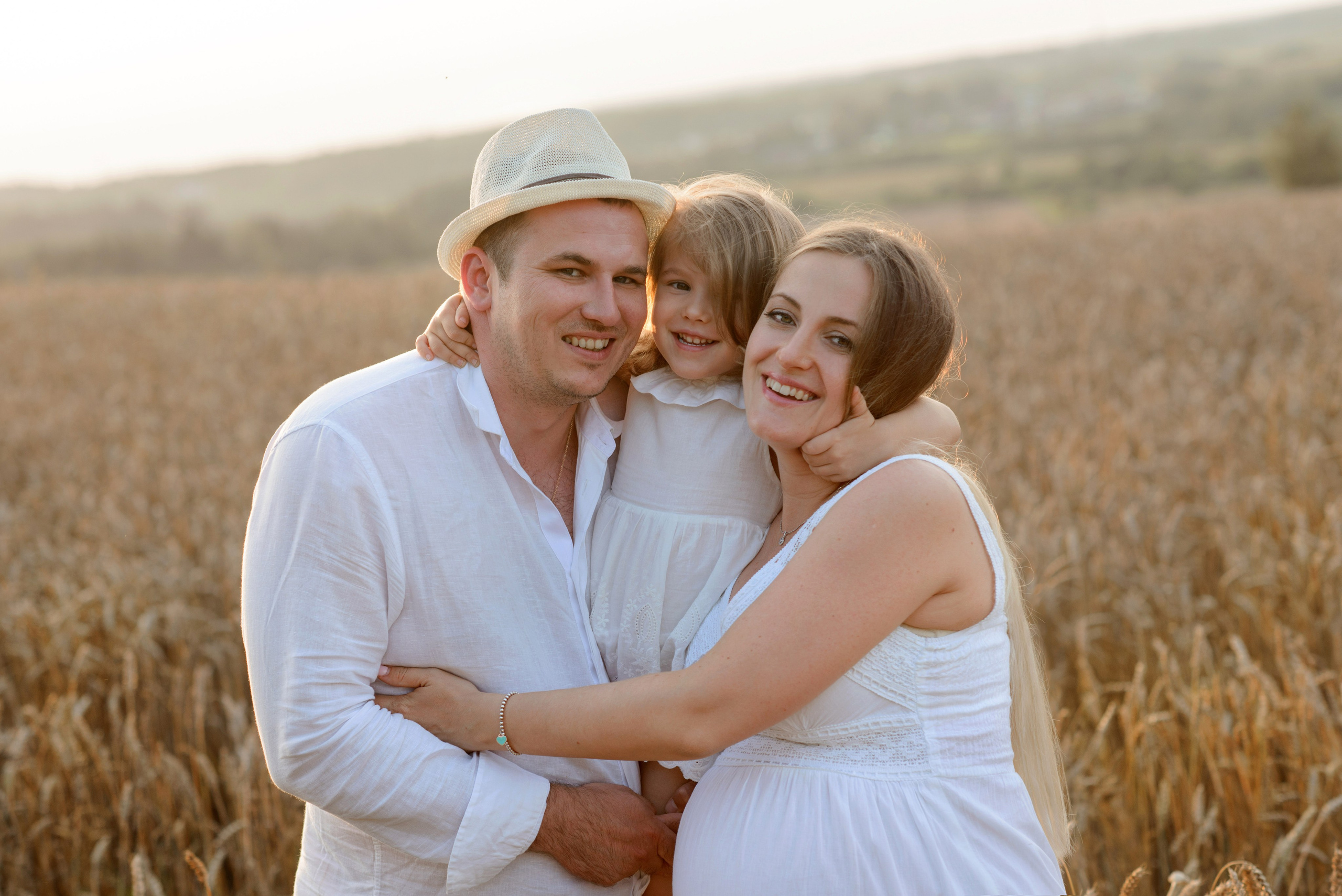 Family photo shoot, pregnant woman in a wheat field at sunset