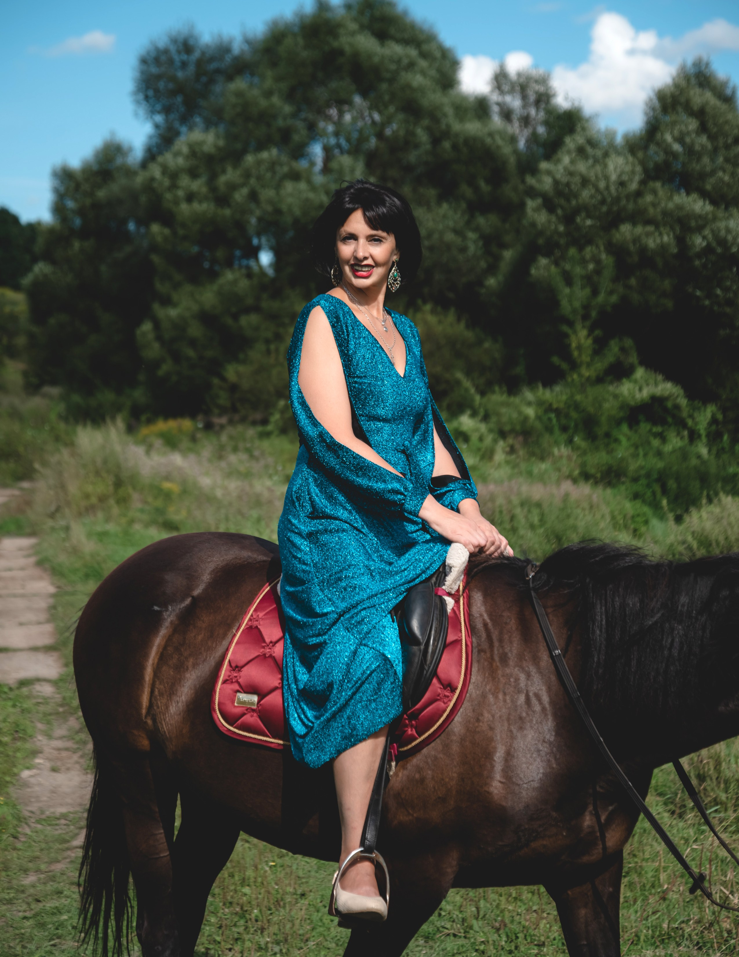 На фото женщина в изумрудном платье сидит на лошади.