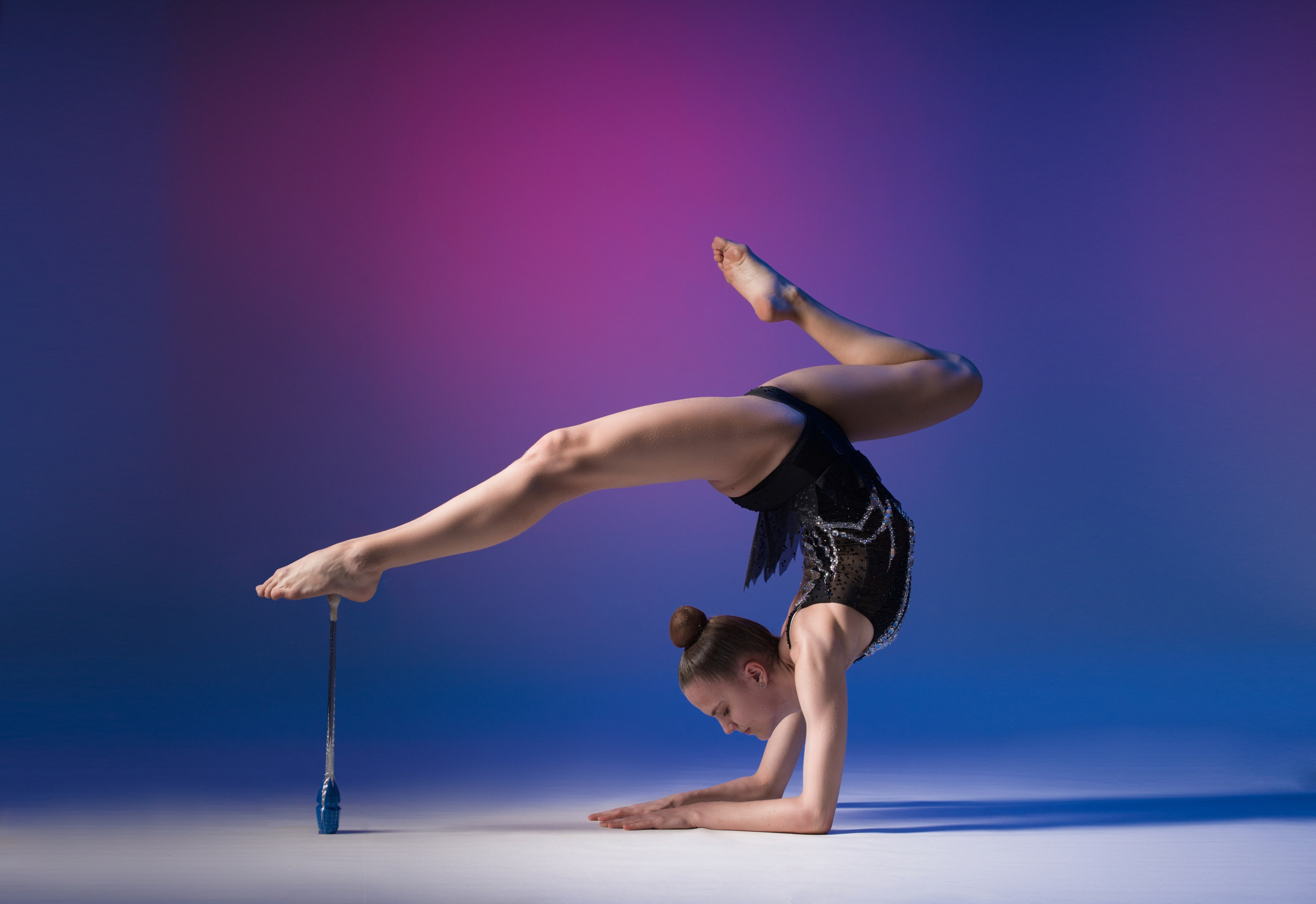 Художественная гимнастка в стойке на предплечьях с булавой, профессиональная арт-съемка в сине-фиолетовых тонах