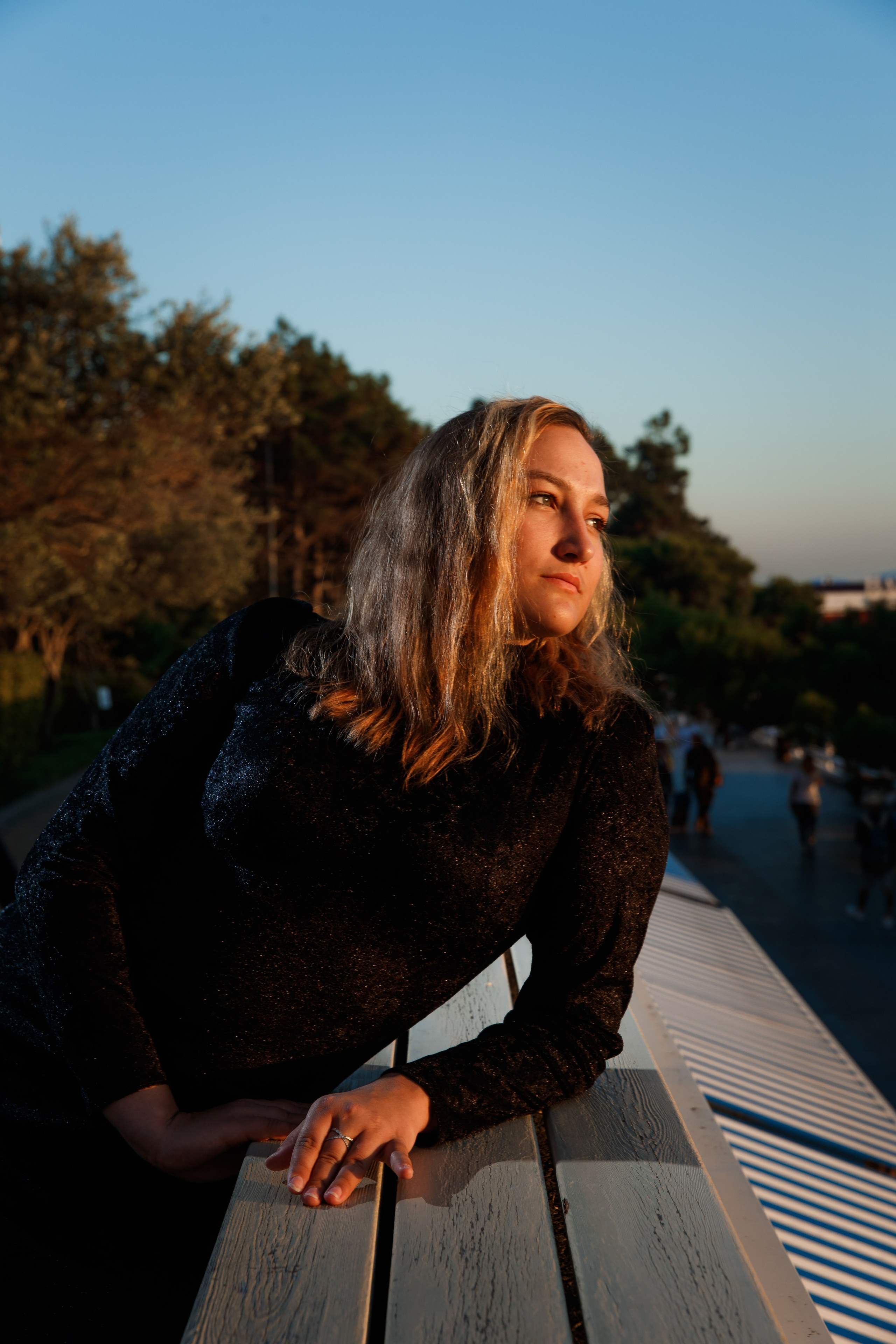 Молодая девушка в чёрном платье смотрит на закатное солнце, облокотившись