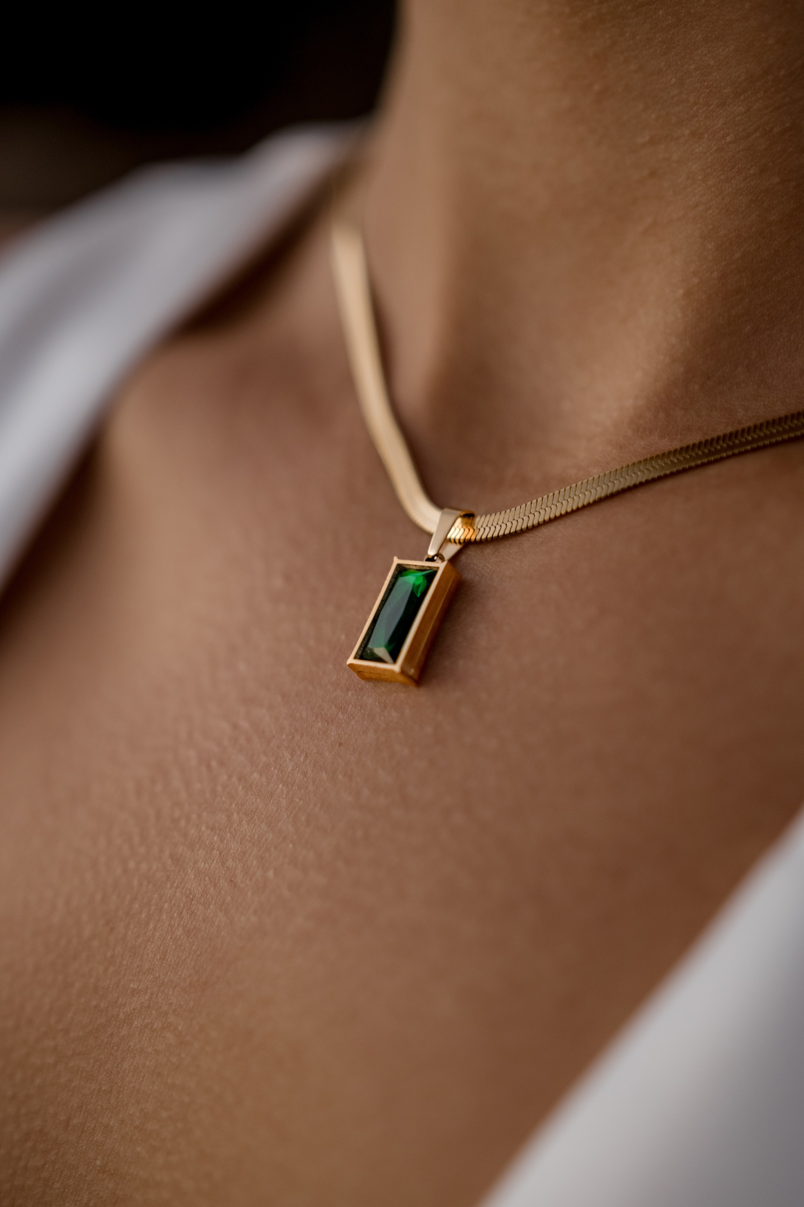Gold necklace with a rectangular emerald pendant styled on a model’s neckline, highlighting refined luxury.