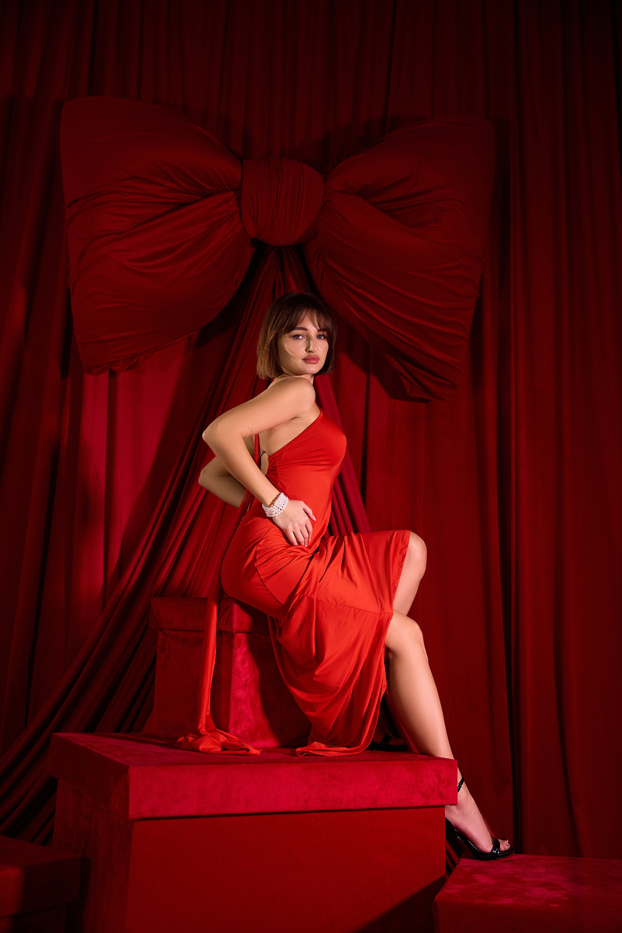 Девушка в красном на красном фоне с бантом, на красных коробках подарочных