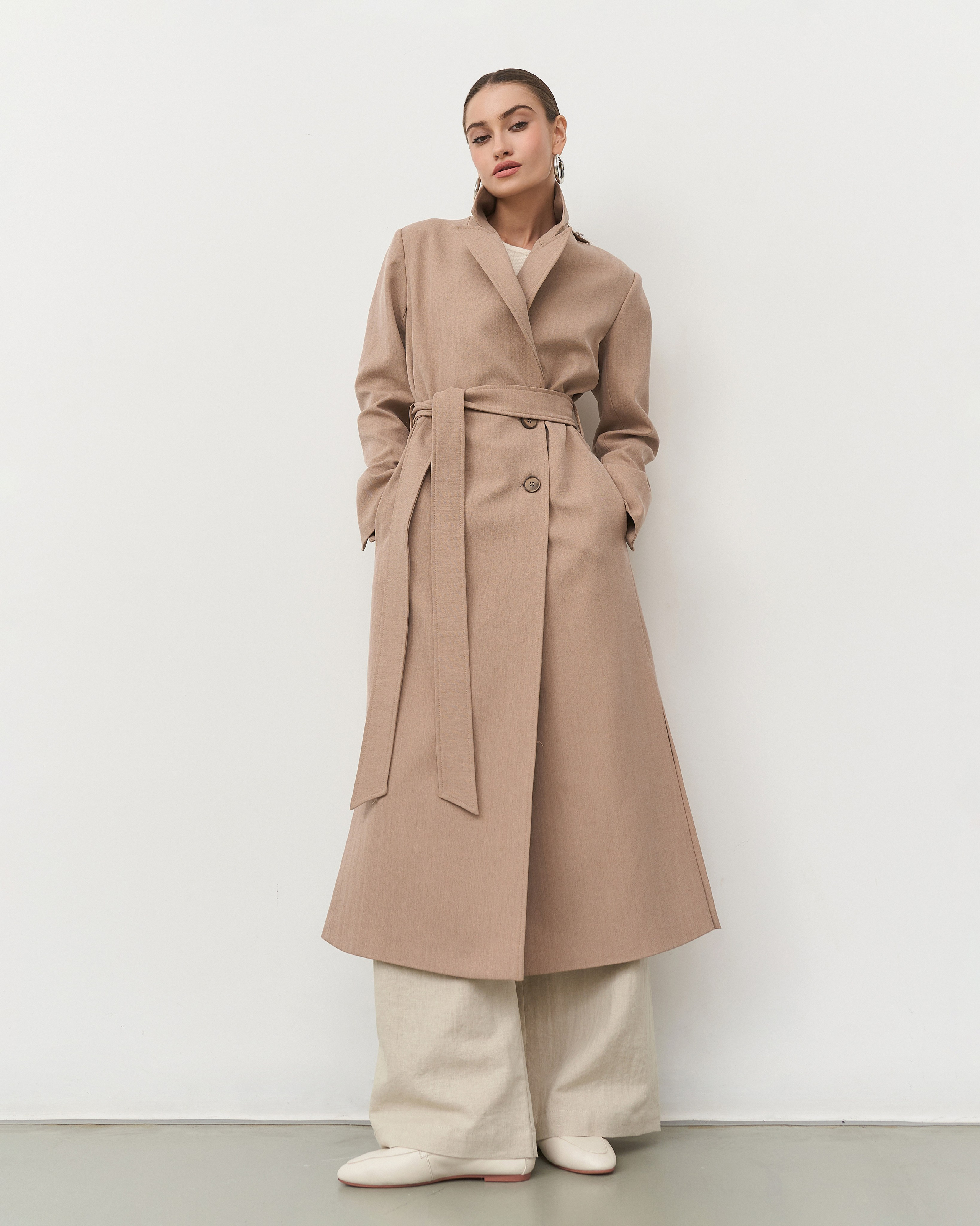 Модель в бежевом пальто с поясом с ракурса снизу