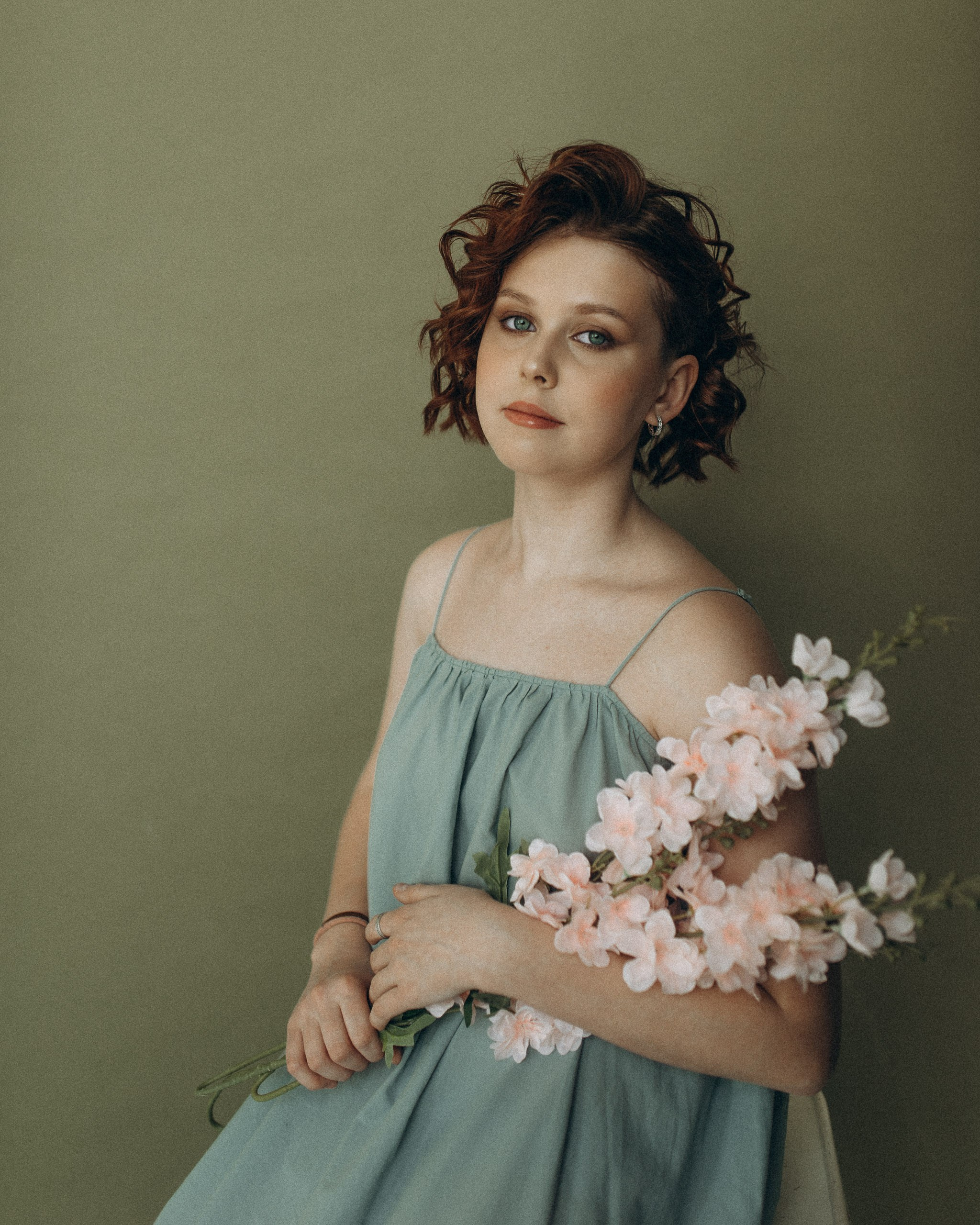 Эстетичный портрет девушки с цветами в руках. Короткая рыжая стрижка, голубое платье и оливковый фон. Профессиональная фотосессия в подарок
