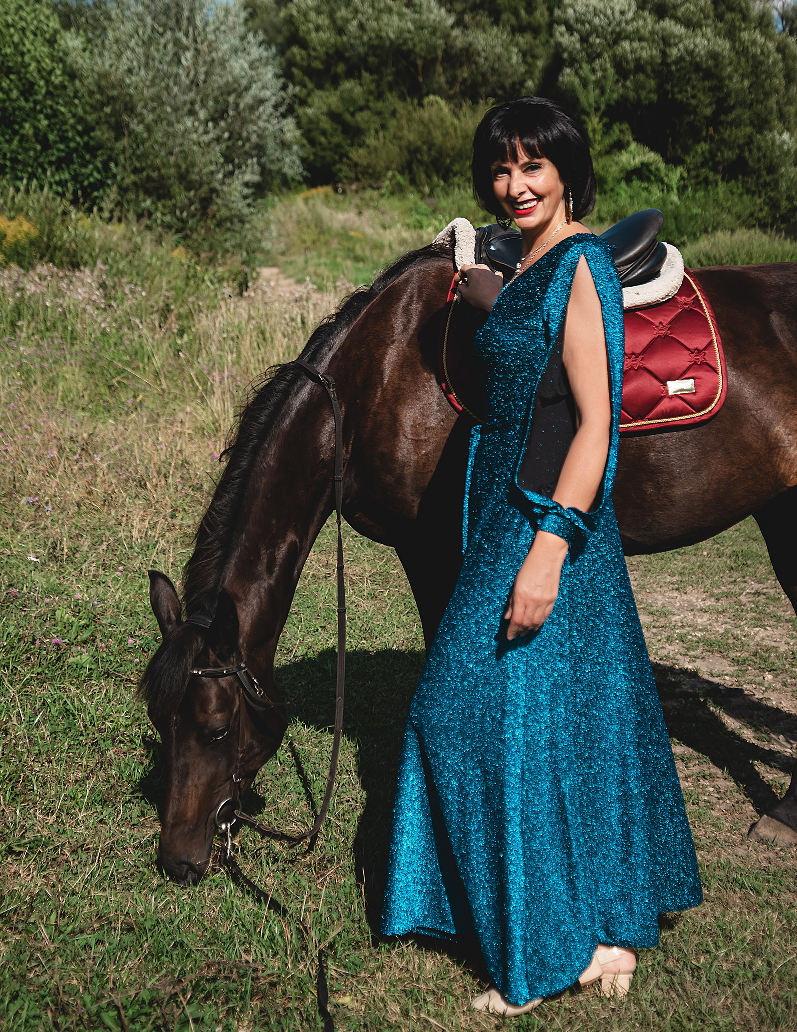 На фото женщина в зеленом платье стоит с лошадью и гладит ее.