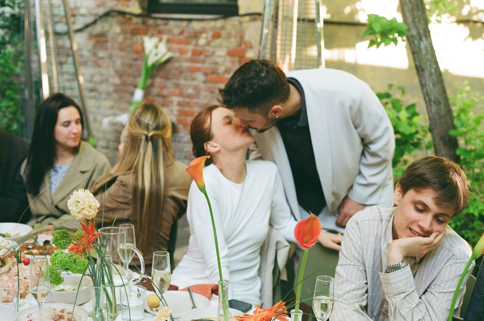 Жених наклоняется к Марии за столом, плёночная текстура Gold 200 создаёт уют