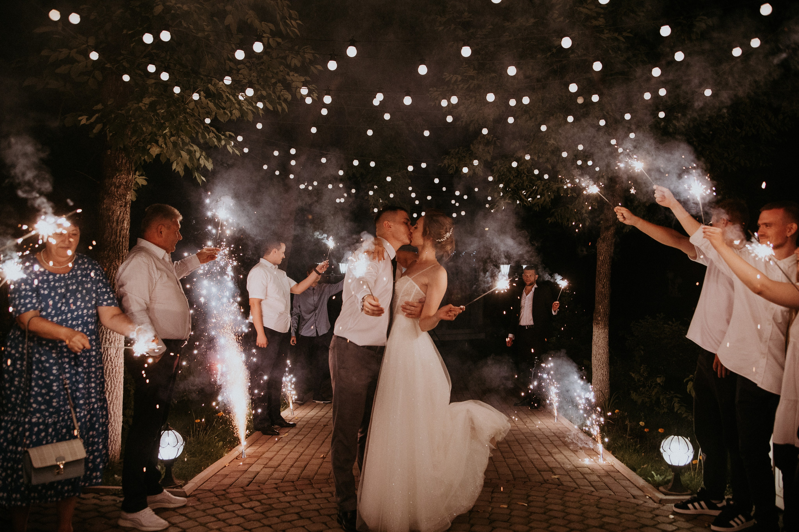 Молодожены целуются в окружении гостей на финале свадьбы с бенгальскими огнями