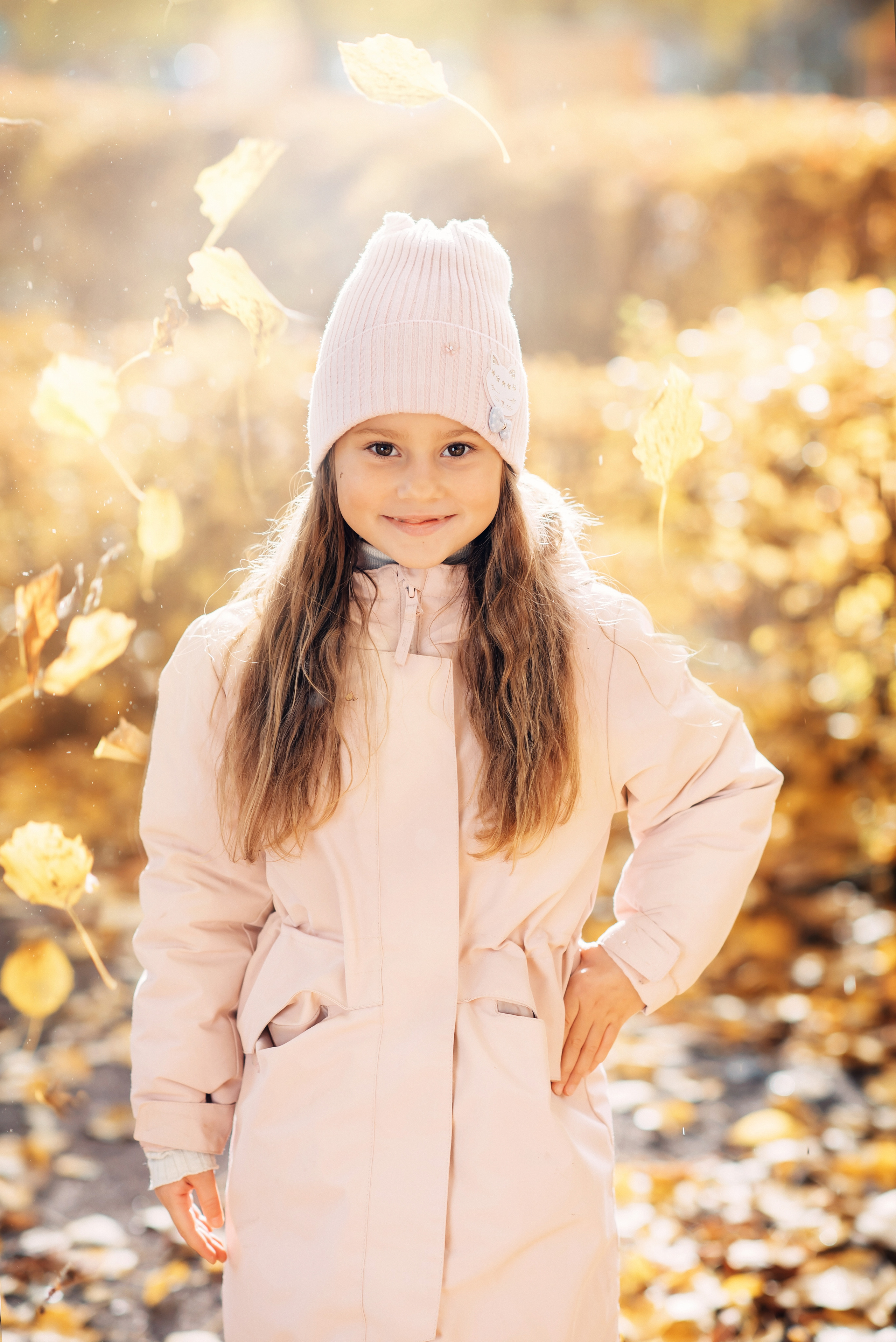 Девочка стоит в саду детского сада на фоне осенних листьев и яркого солнца