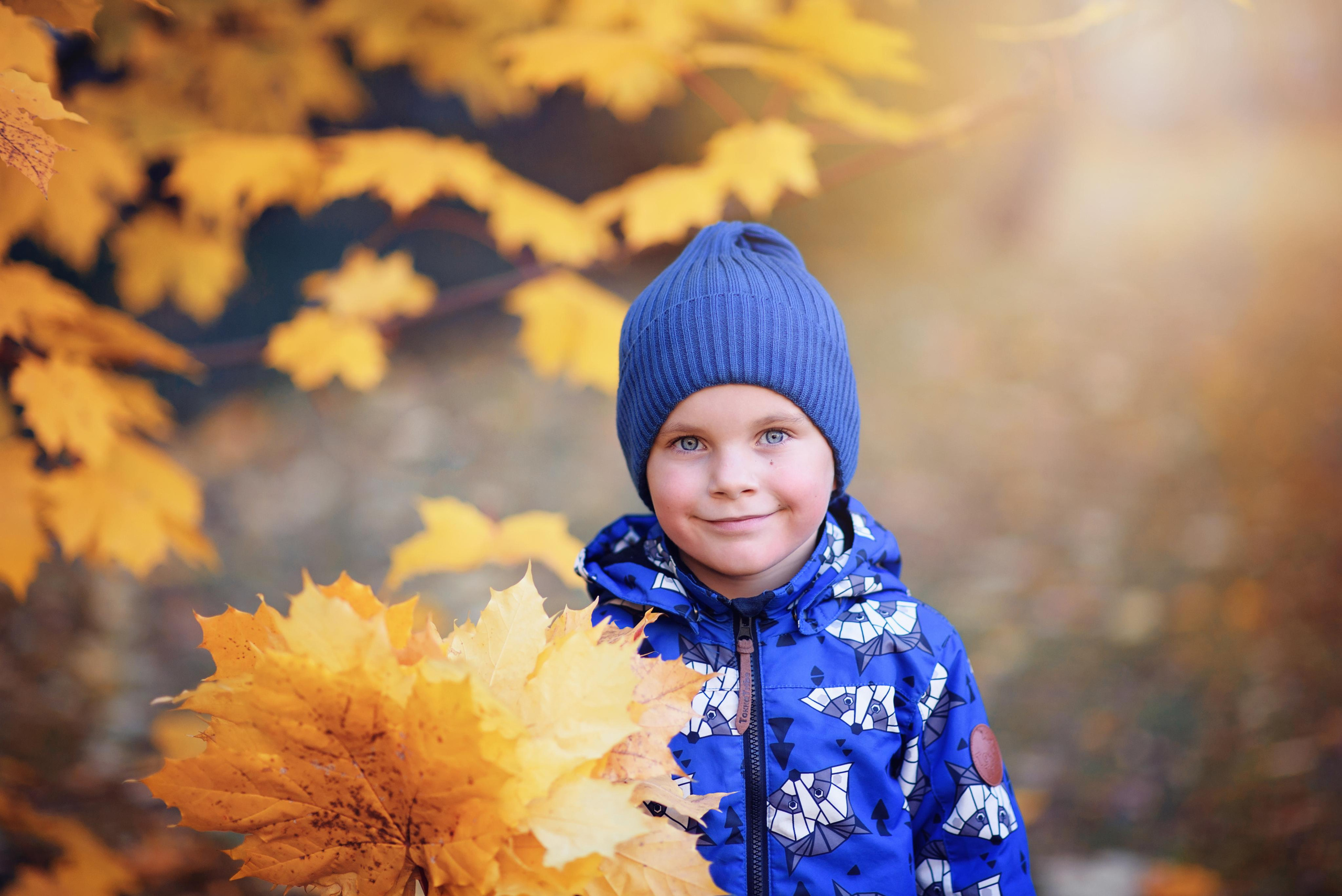 Мальчик стоит во дворе детского сада с букетом осенних листьев в руках фотографируясь для выпускной фотокниги