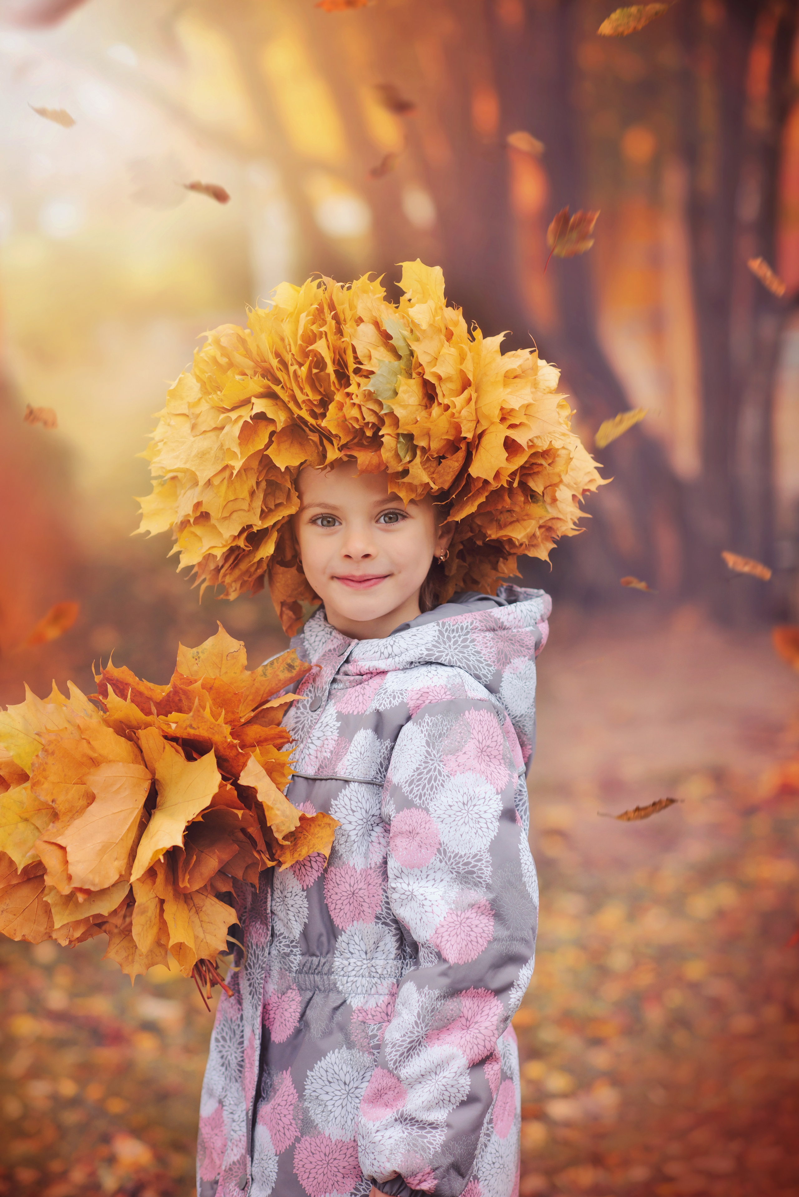 Девочка стоит во дворе детского сада с букетом осенних листьев в руках фотографируясь для выпускного альбома
