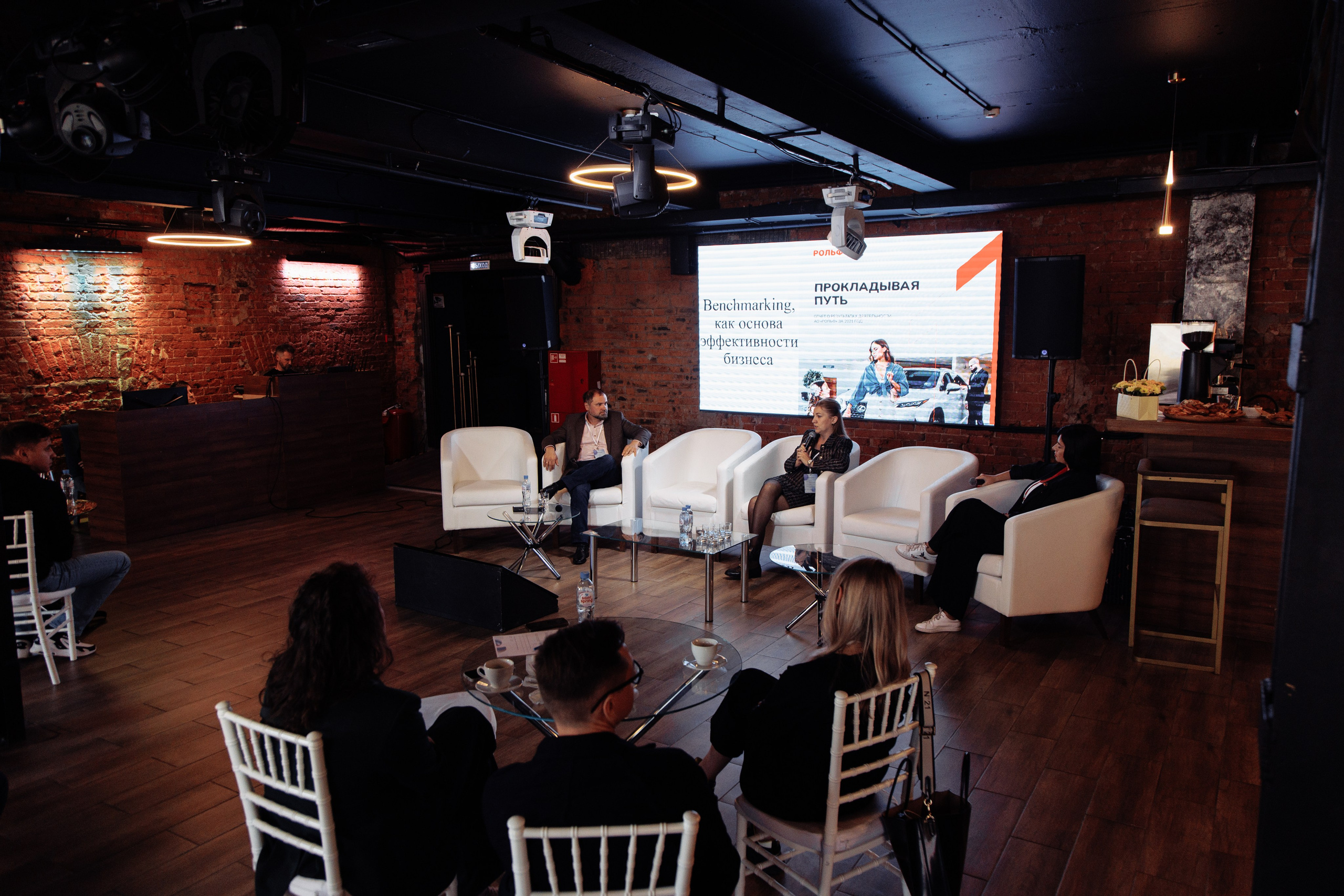 Репортажное фото: несколько спикеров ведут дискуссию или панель на сцене.