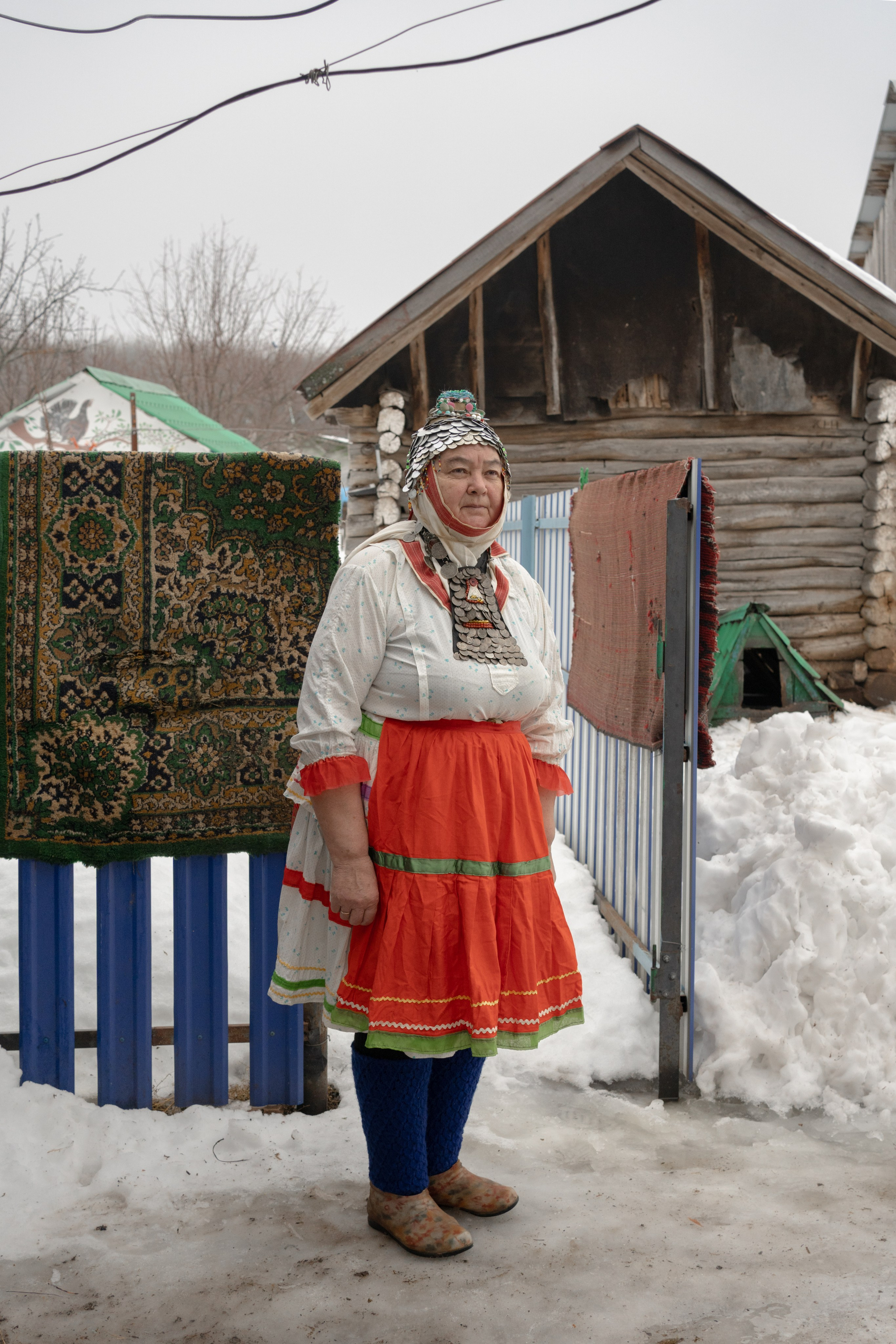 Лидия Викторовна Молянова во дворе своего дома. На Лидии Викторовне ее традиционный чувашский костюм. На головном уборе замужней женщины хушпу и традиционном женском нагрудном украшении старинные монеты начала 20 века. Этот костюм перешел Лидии Викторовне от ее бабушки. Лидия Викторовна является хранительницей традиционных чувашских обрядов. Когда в селе умирает человек местные жители обращаются к ней для подготовки к обряду погребения. Село Староганькино, Самарская область, декабрь 2023 год.
