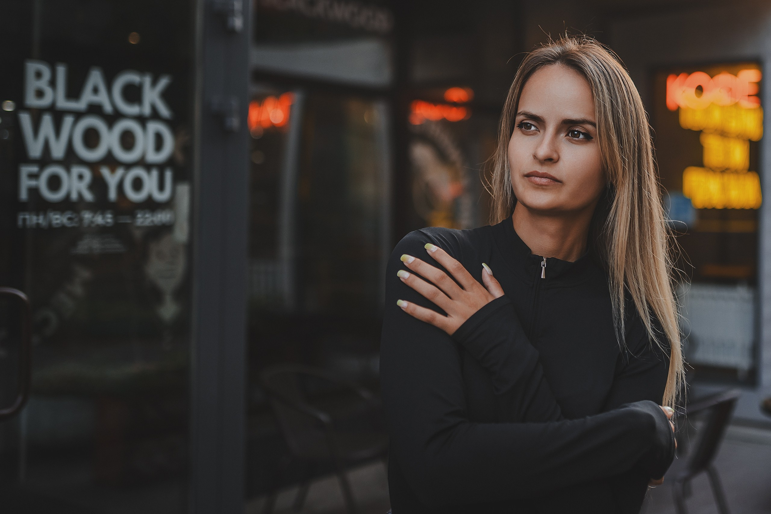 Атмосферный уличный портрет. Молодая женщина у входа в городское кафе с неоновыми вывесками. Вечерняя съемка.