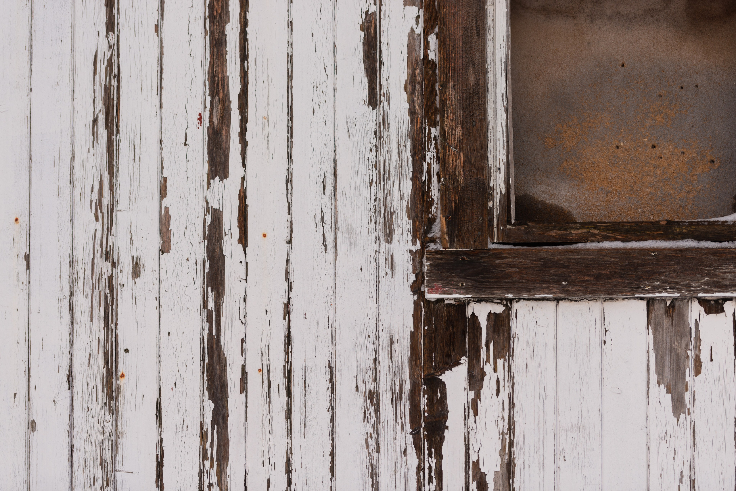 Крупный план старой деревянной обшивки здания с сильно облупившейся белой краской и частью темной оконной рамы.