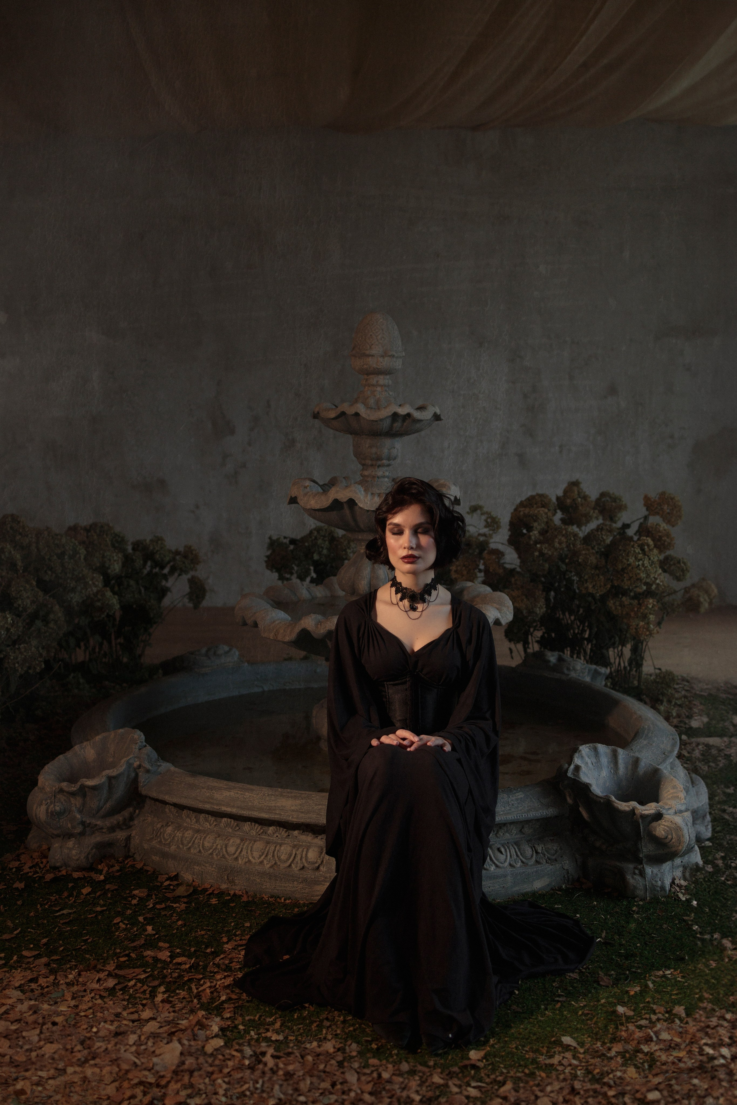 Девушка сидит на краю фонтана, руки сложены на коленях, глаза закрыты