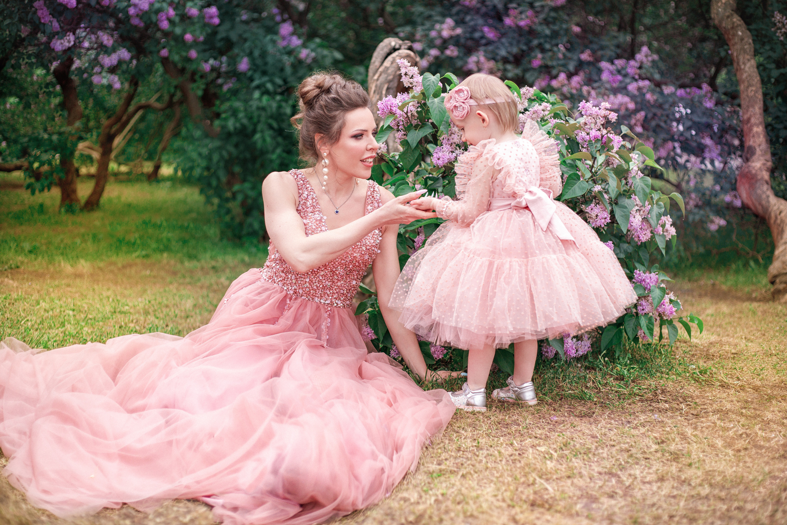 Мама и дочка в розовых платьях фотографируются на фоне сиреневых деревьев