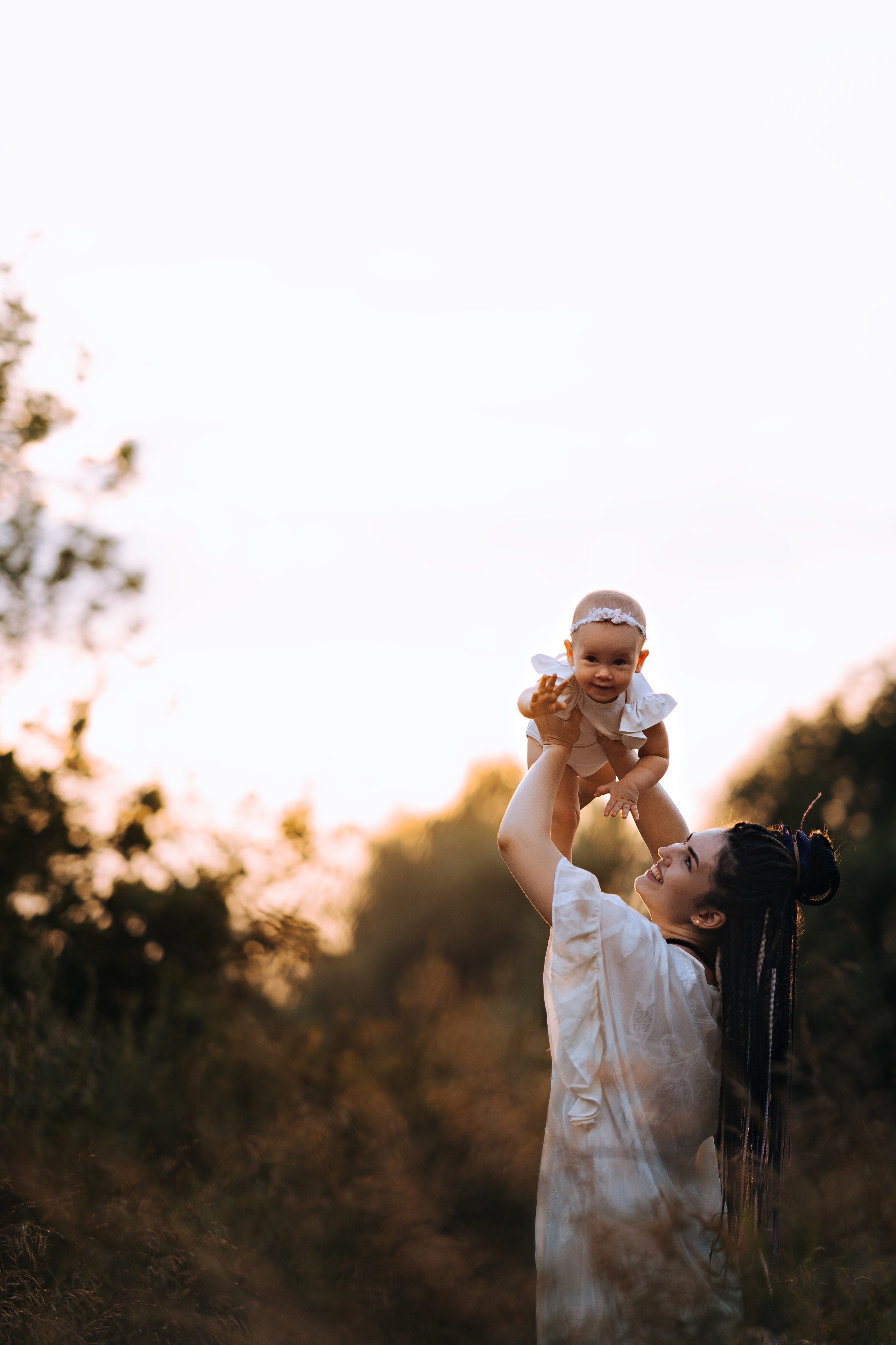 Счастливая мама на природе подбрасывает свою малышку в воздух, та улыбается