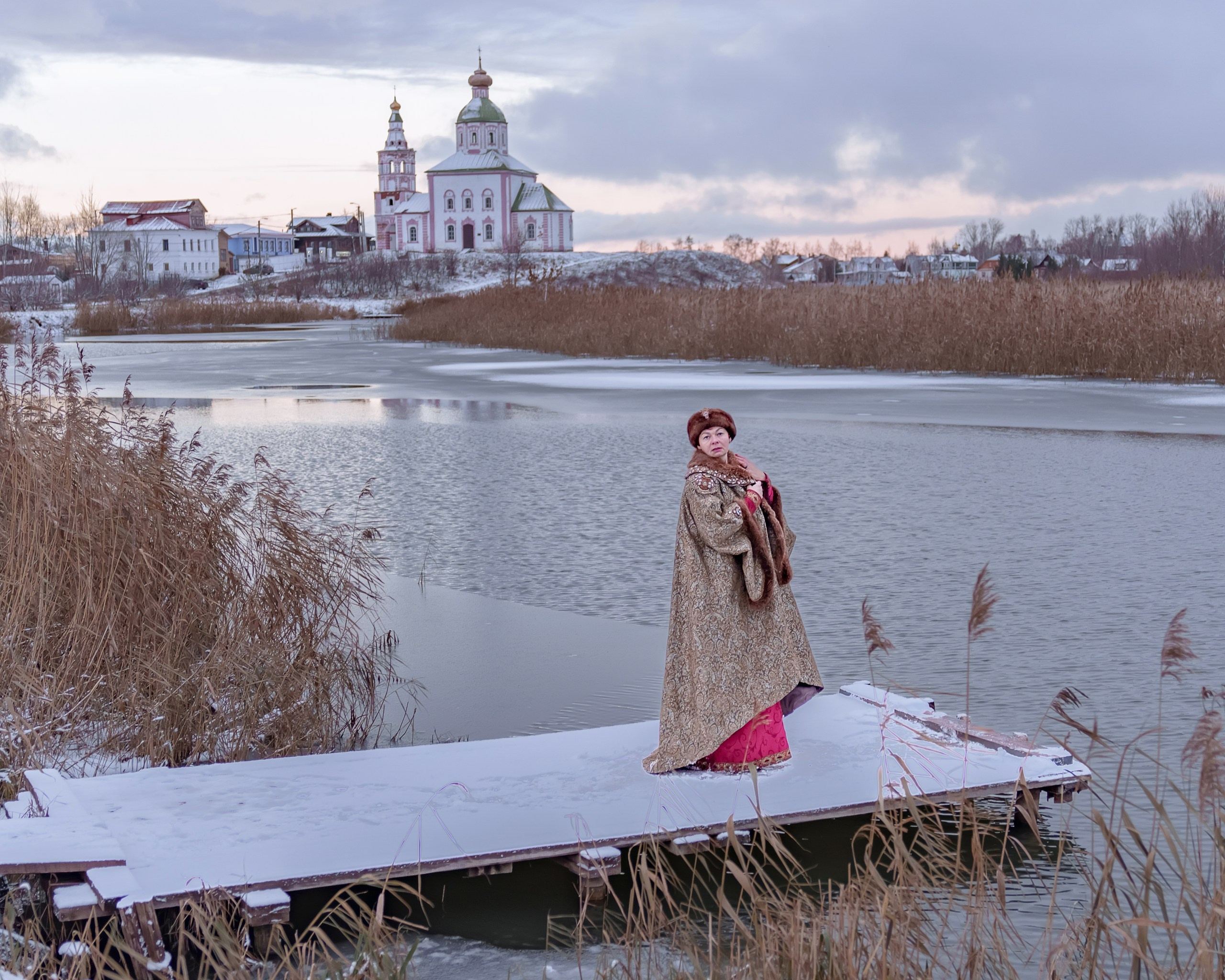 A girl in a boyar costume on the background of a temple in Suzdal by the river