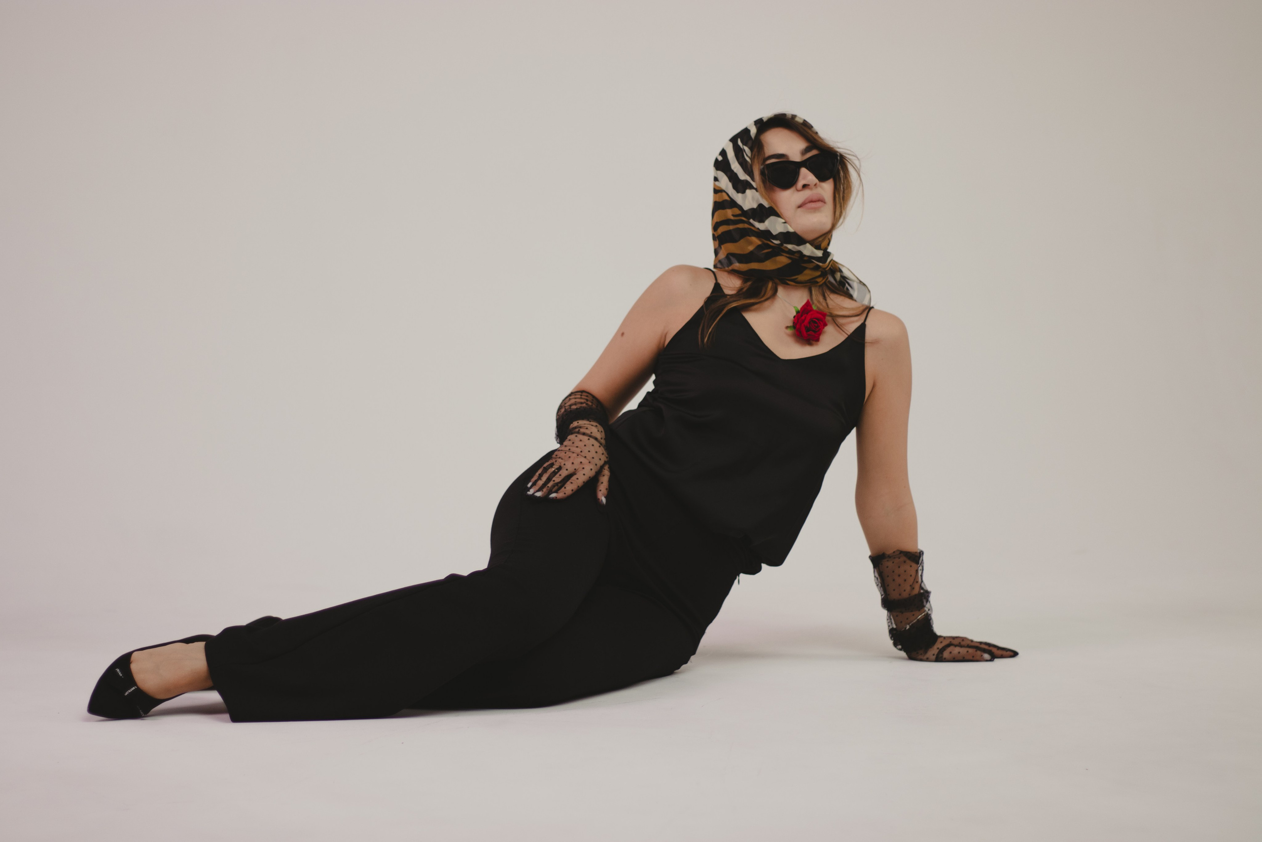 Портрет девушки в полный рост, которая лежит на белой циклораме в черной одежде и ярко красной розой на шее