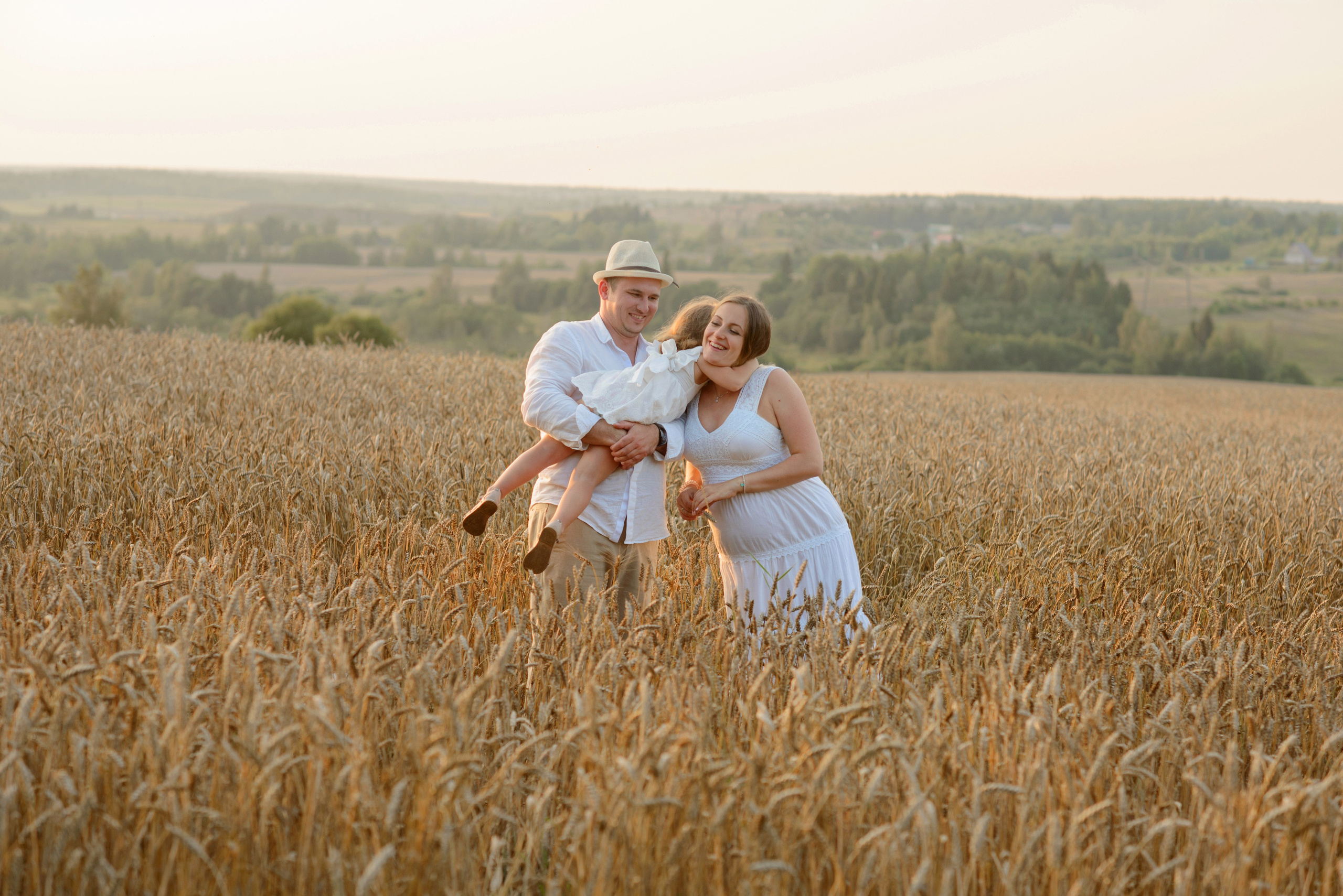Family photo shoot, pregnant woman in a wheat field at sunset
