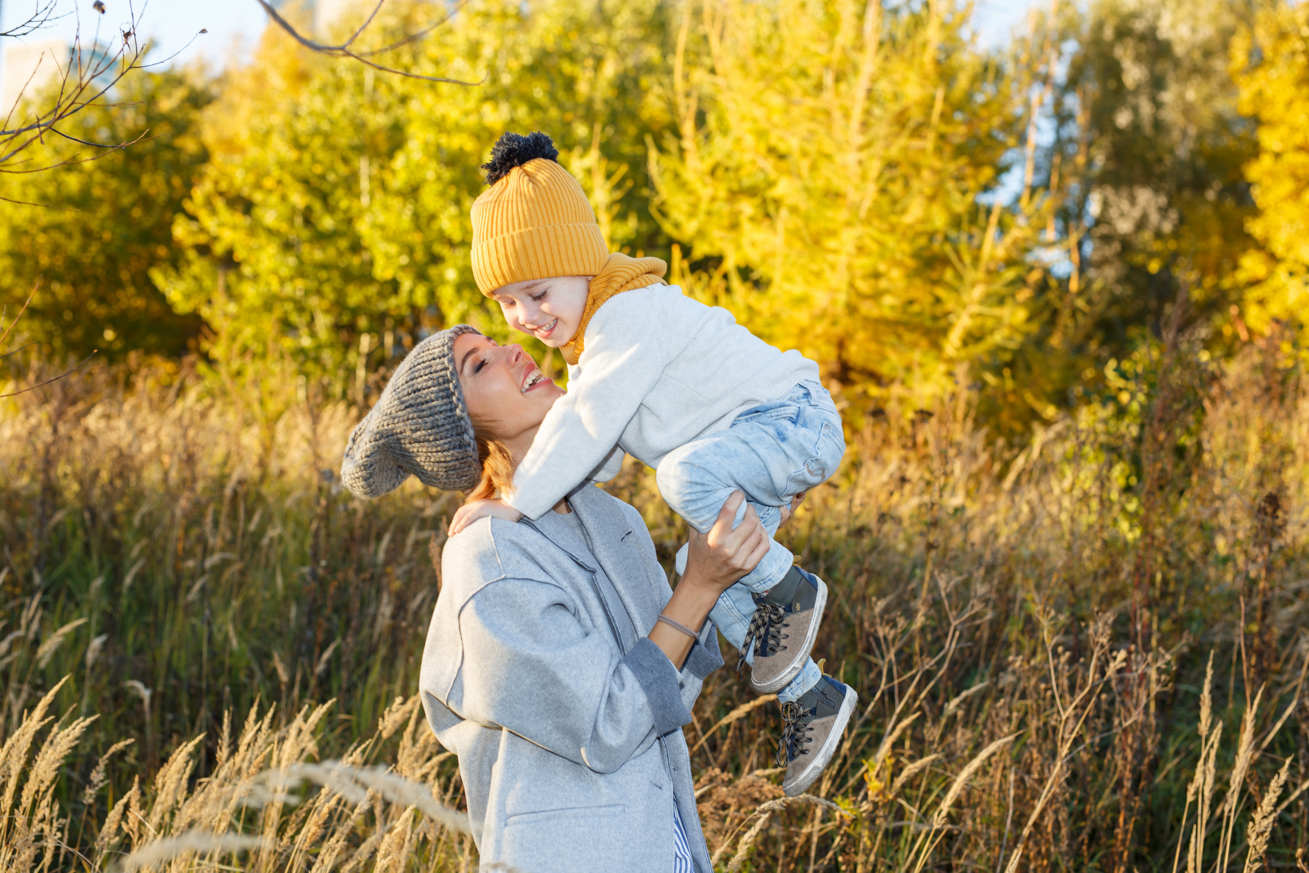 Красивая мама целует маленького сына во время фотосессии на фоне осеннего дерева
