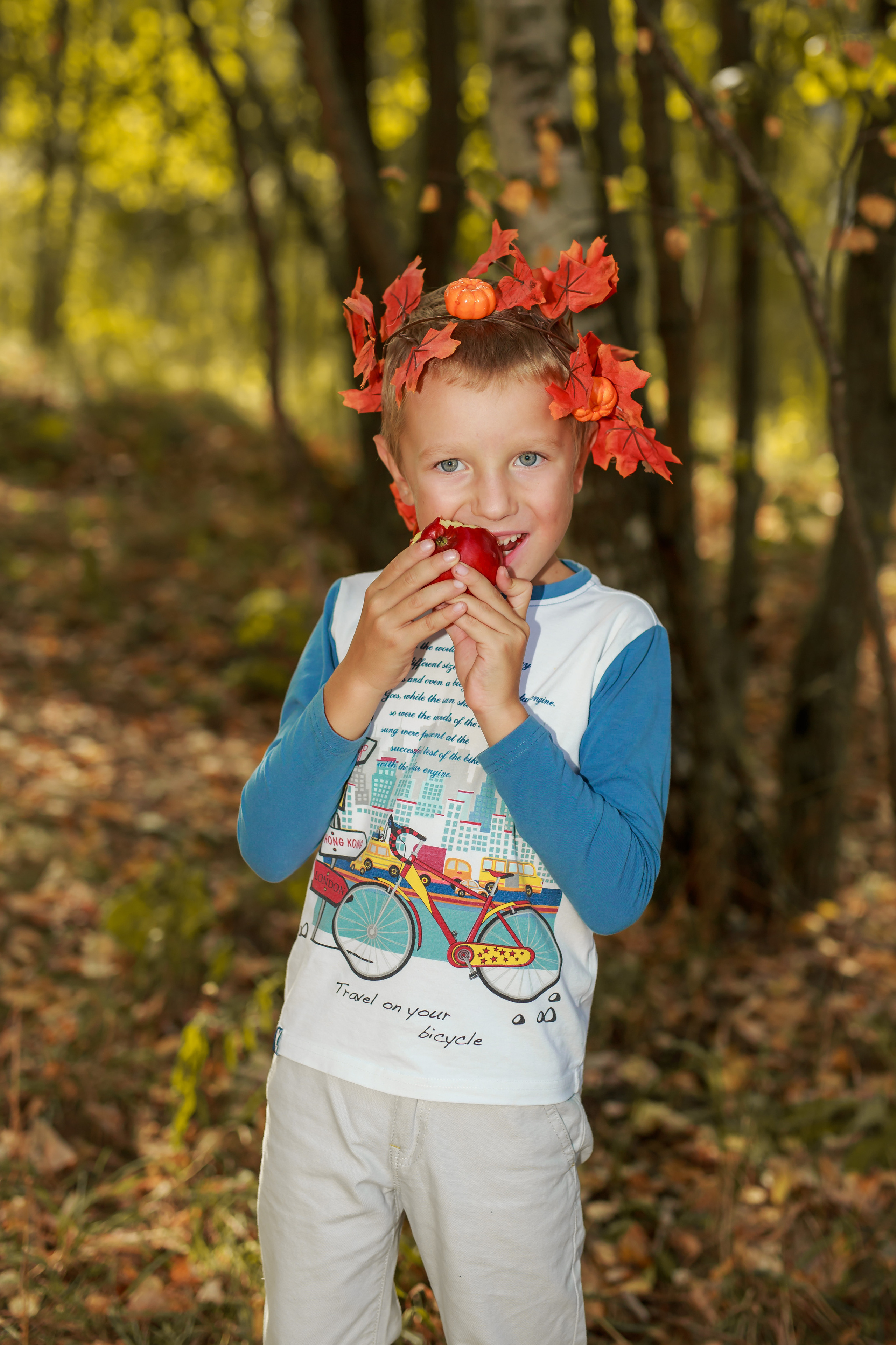 Мальчик кушает вкусное красное яблоко на фоне золотой осени