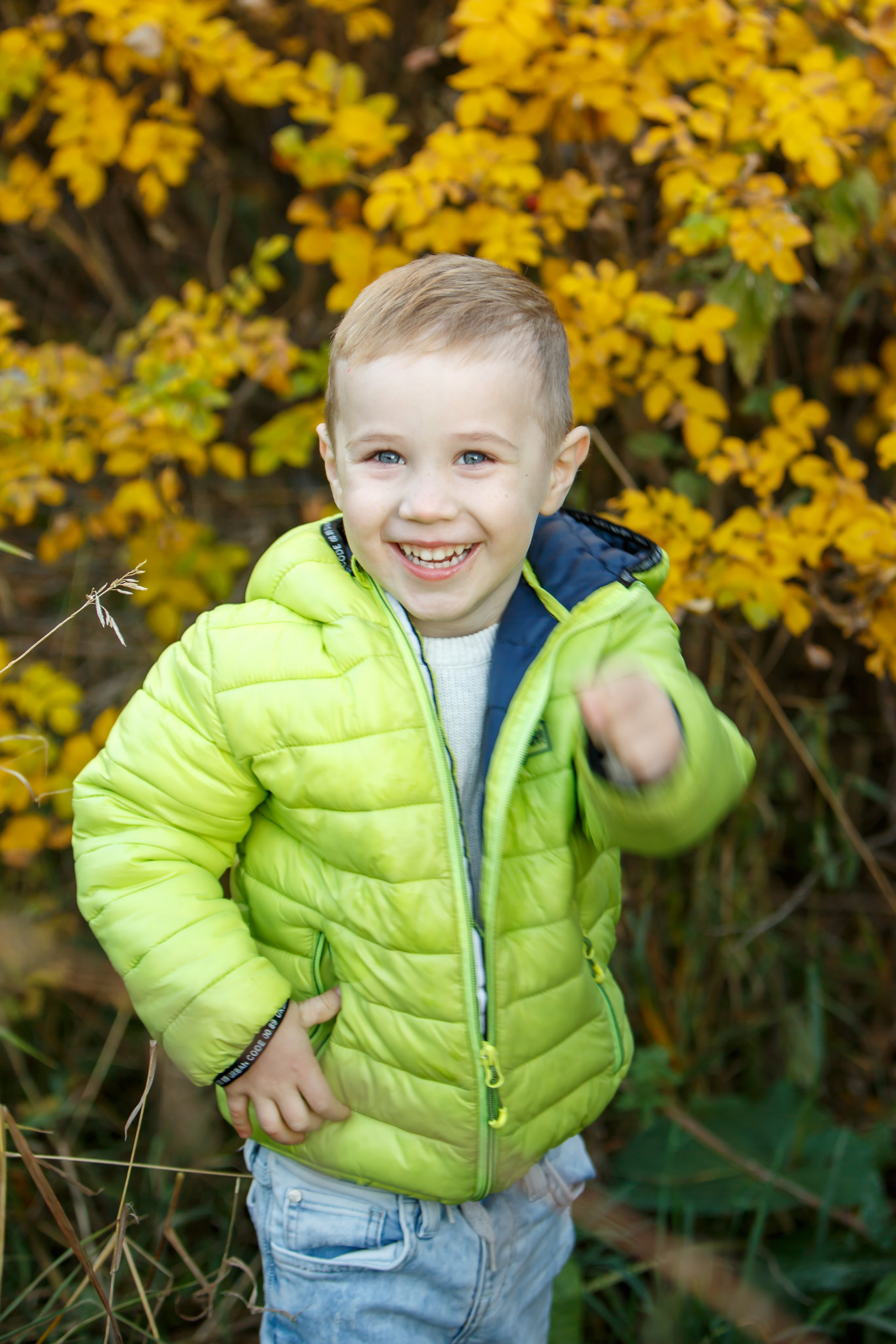 Веселый мальчик в желтой куртке играет с осенними листьями