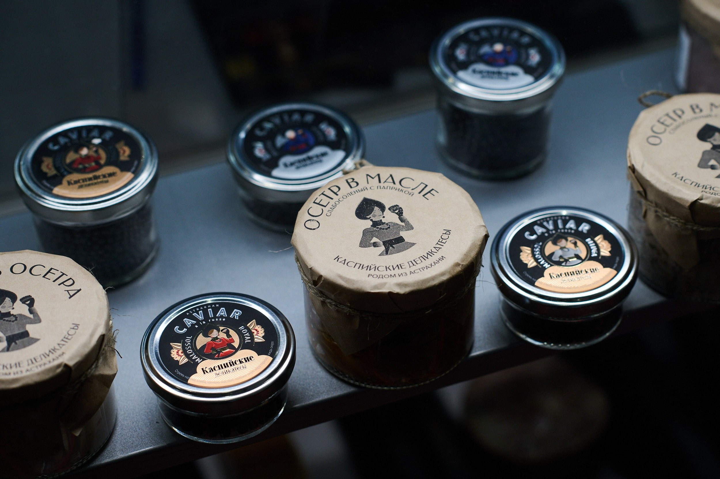 Полка с банками «Осетр в масле» от фирмы «Каспийские деликатесы» на выставке Seafood Expo Russia 2025. Репортажная съёмка экспозиции в КВЦ «Экспофорум», Санкт‑Петербург.