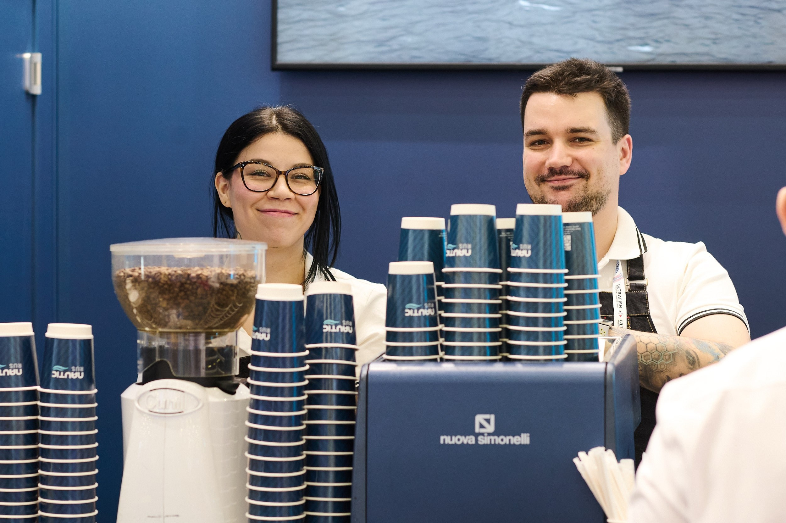 Баристы улыбаются в камеру на стенде Nautic Rus. Seafood Expo Russia 2025, репортажная съёмка, Экспофорум, Санкт‑Петербург.