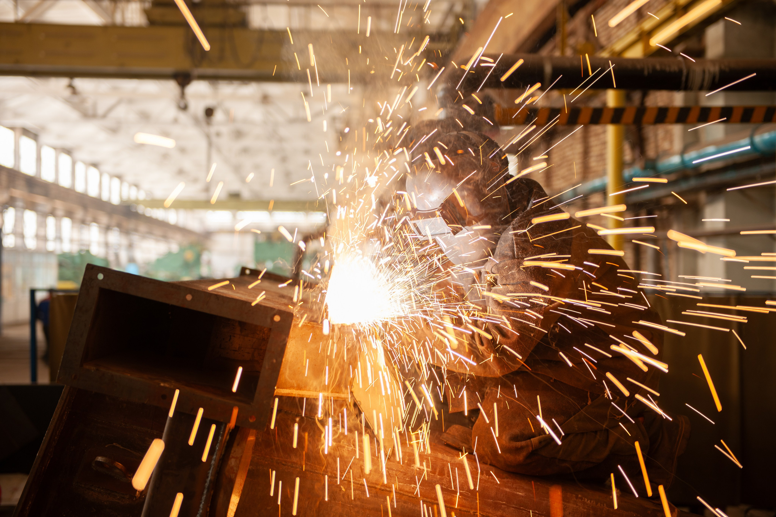 Сварка металла с летящими искрами — промышленная фотосъёмка работы сотрудников на производстве