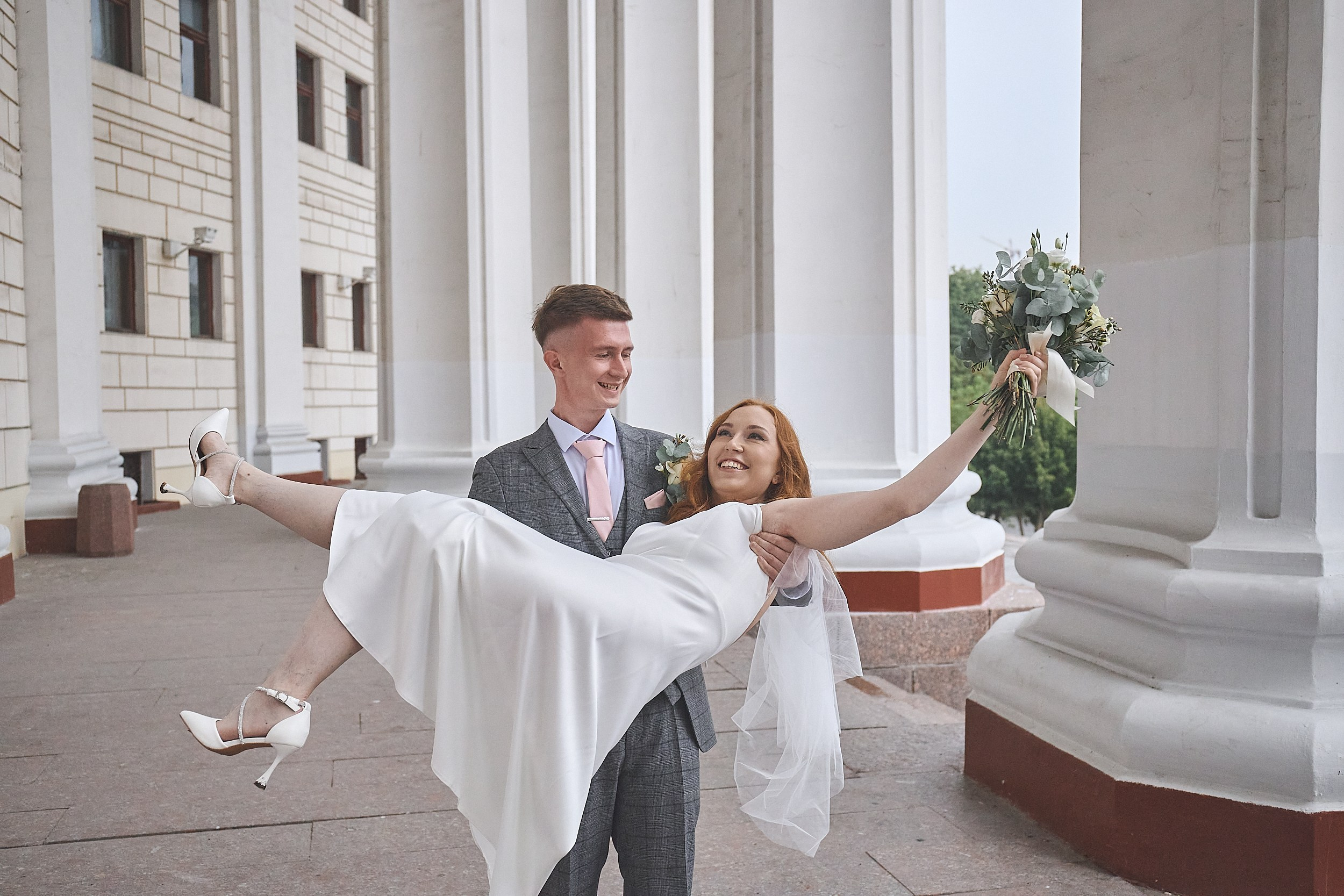 Молодой жених держит на курках свою невесту на фоне колон Театра Армии России