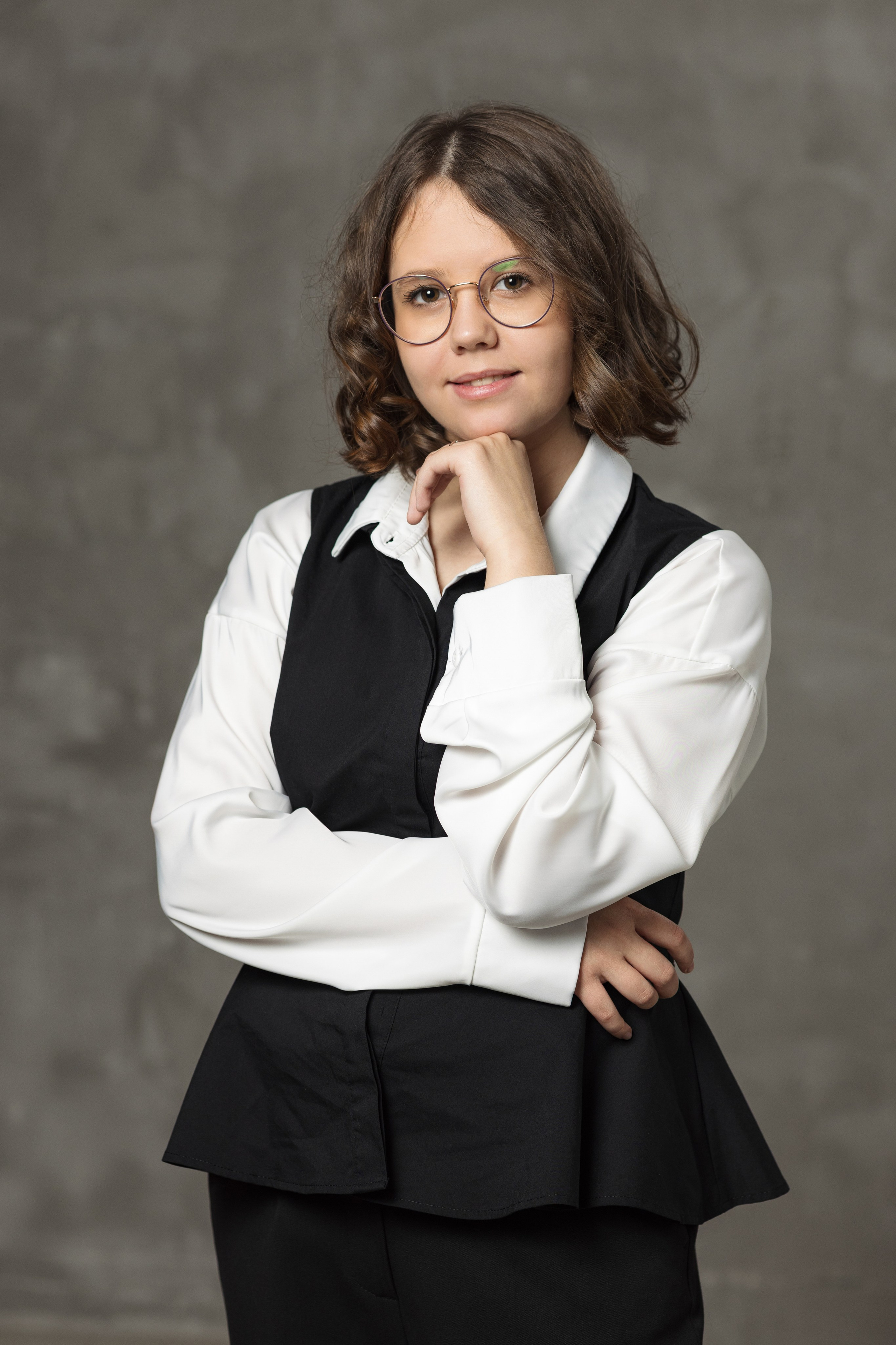 Девушка в белой рубашке и тёмном жилете снята в студийном портрете.