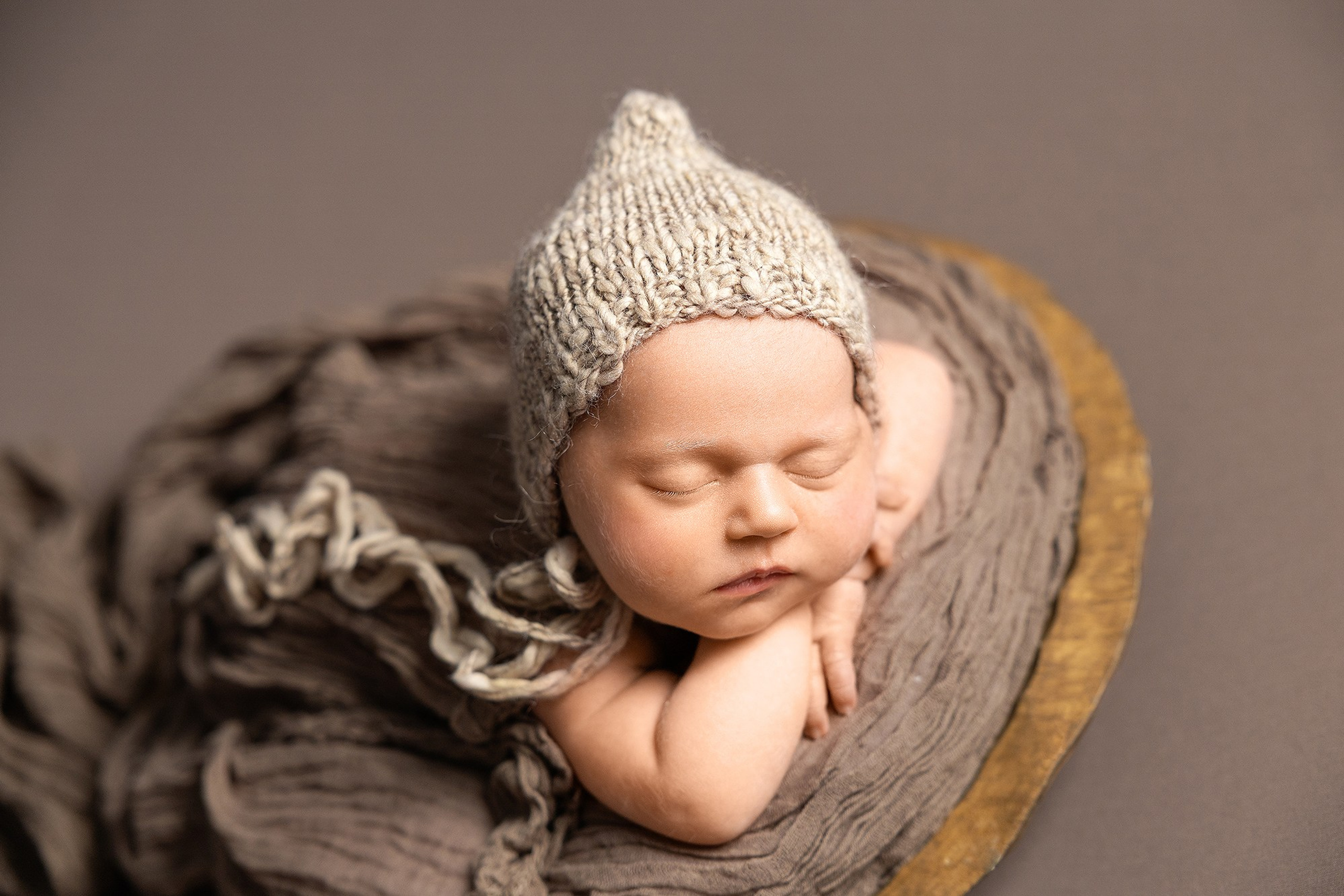 Портрет новорожденного ребенка в шапочке на животике в корзинке.