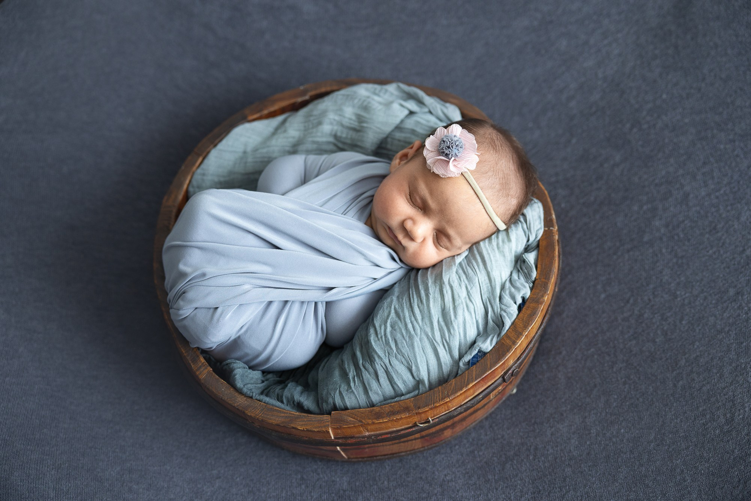 Новорожденный малыш спит в деревянной бадейке, укутанный в мягкую ткань.
