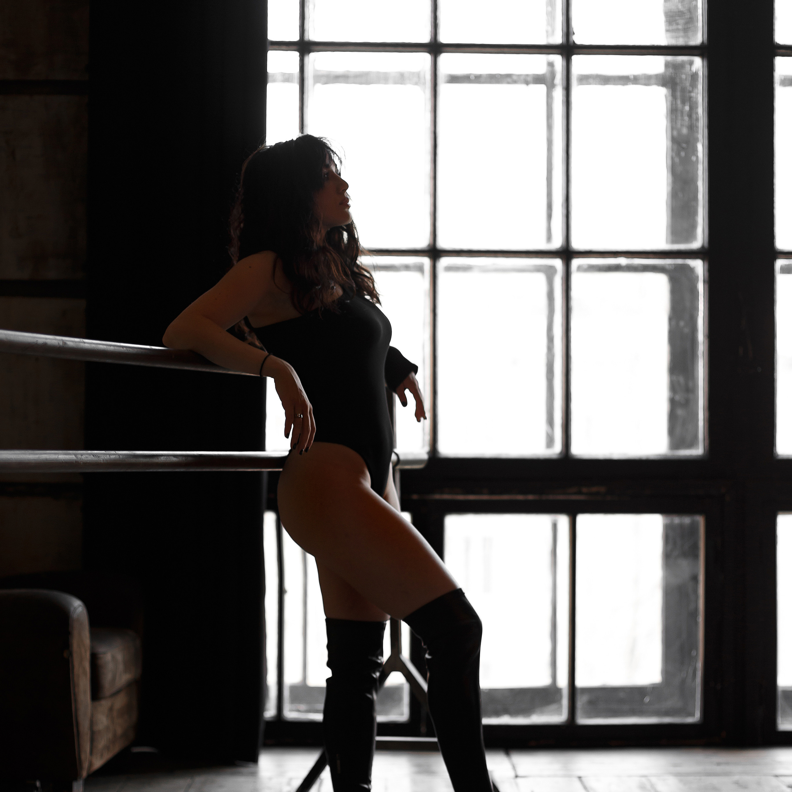 девушка в ботфортах и боди на фоне окна