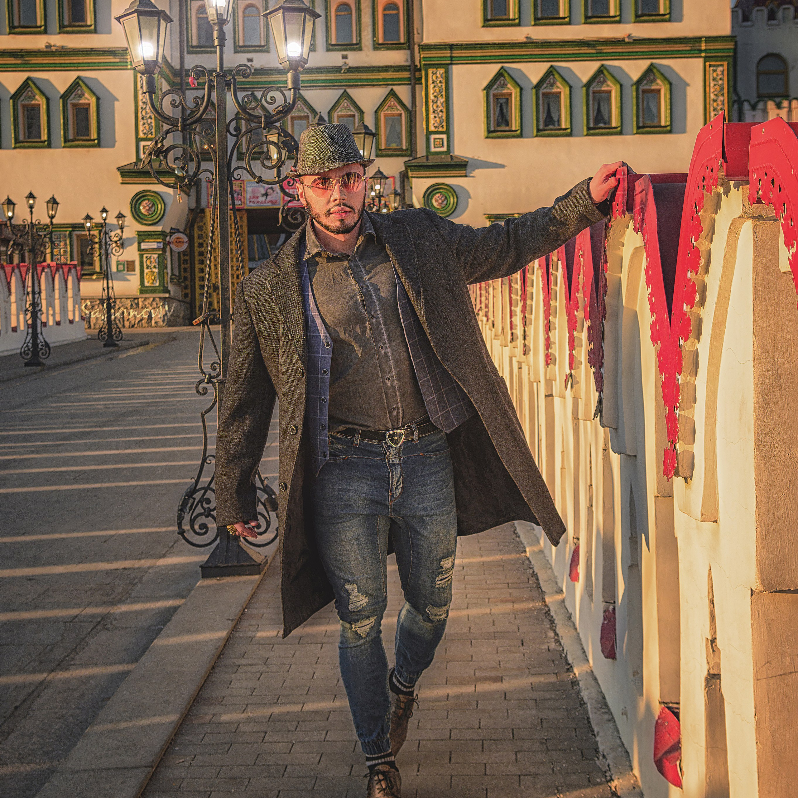 Мужчина в модной одежде и шляпе идет по мосту