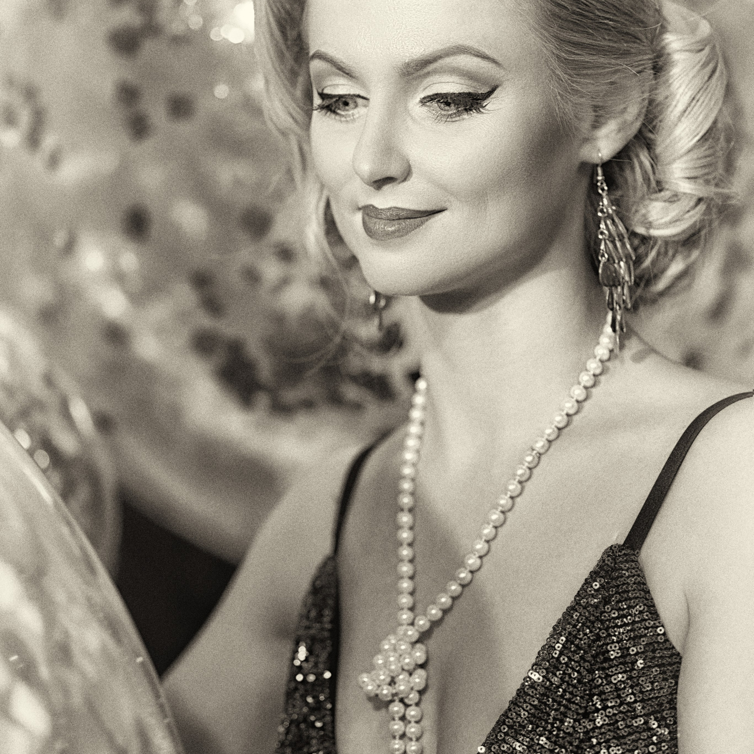 женщина в элегантном платье с глубоким вырезом, украшенном пайетками. Её образ дополняют длинные жемчужные бусы и классические серьги. Волосы уложены в изысканную причёску, а макияж подчёркивает её утончённость. Фон создаёт атмосферу праздника и роскоши.Заголовок: «Элегантность в каждом движении: портрет в стиле ретро»Ключевые слова: портрет, элегантность, жемчужные украшения, классика, ретро стиль, фотосессия, фотограф Сафронов Иван, Москва.