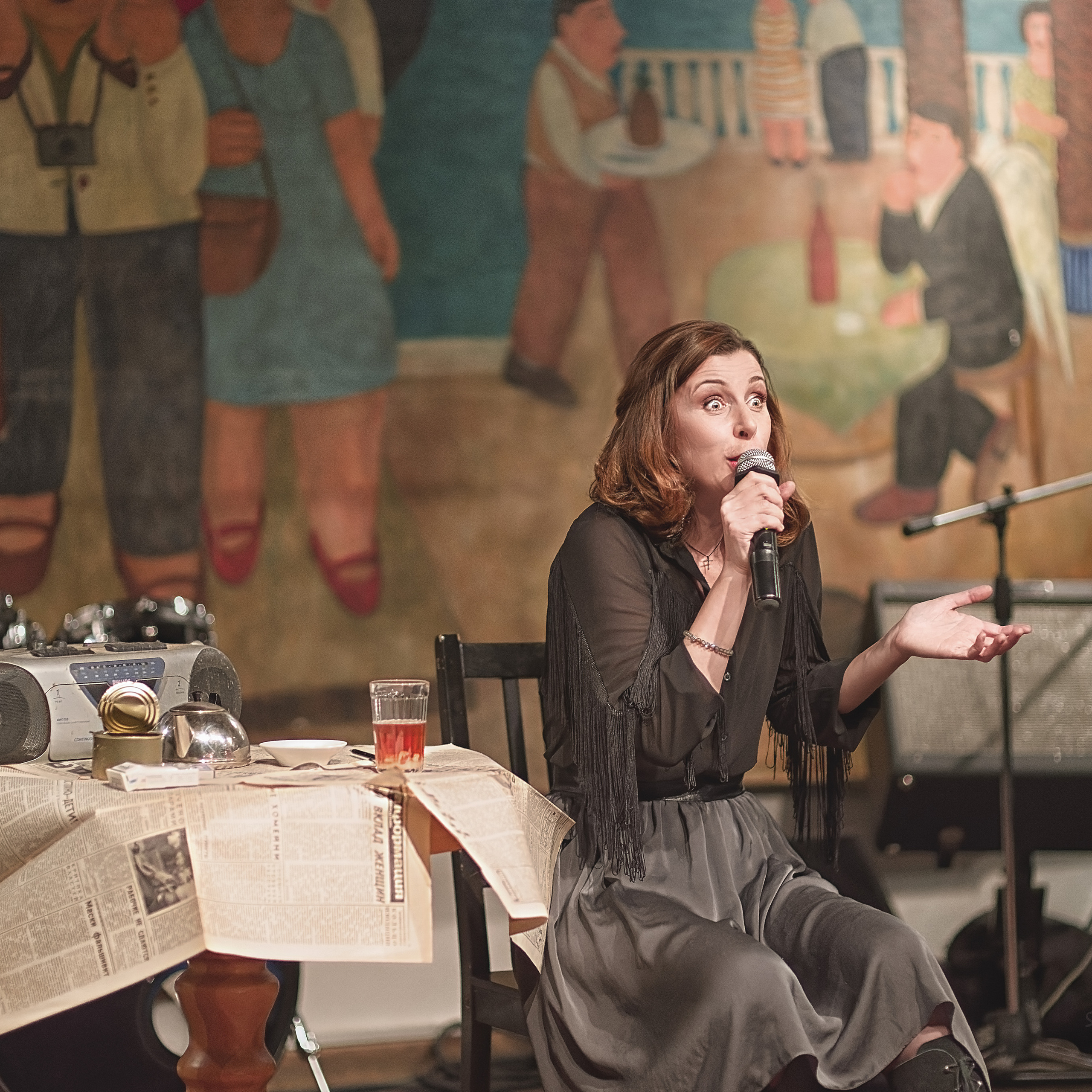 Женщина с микрофоном возле стола на сцене