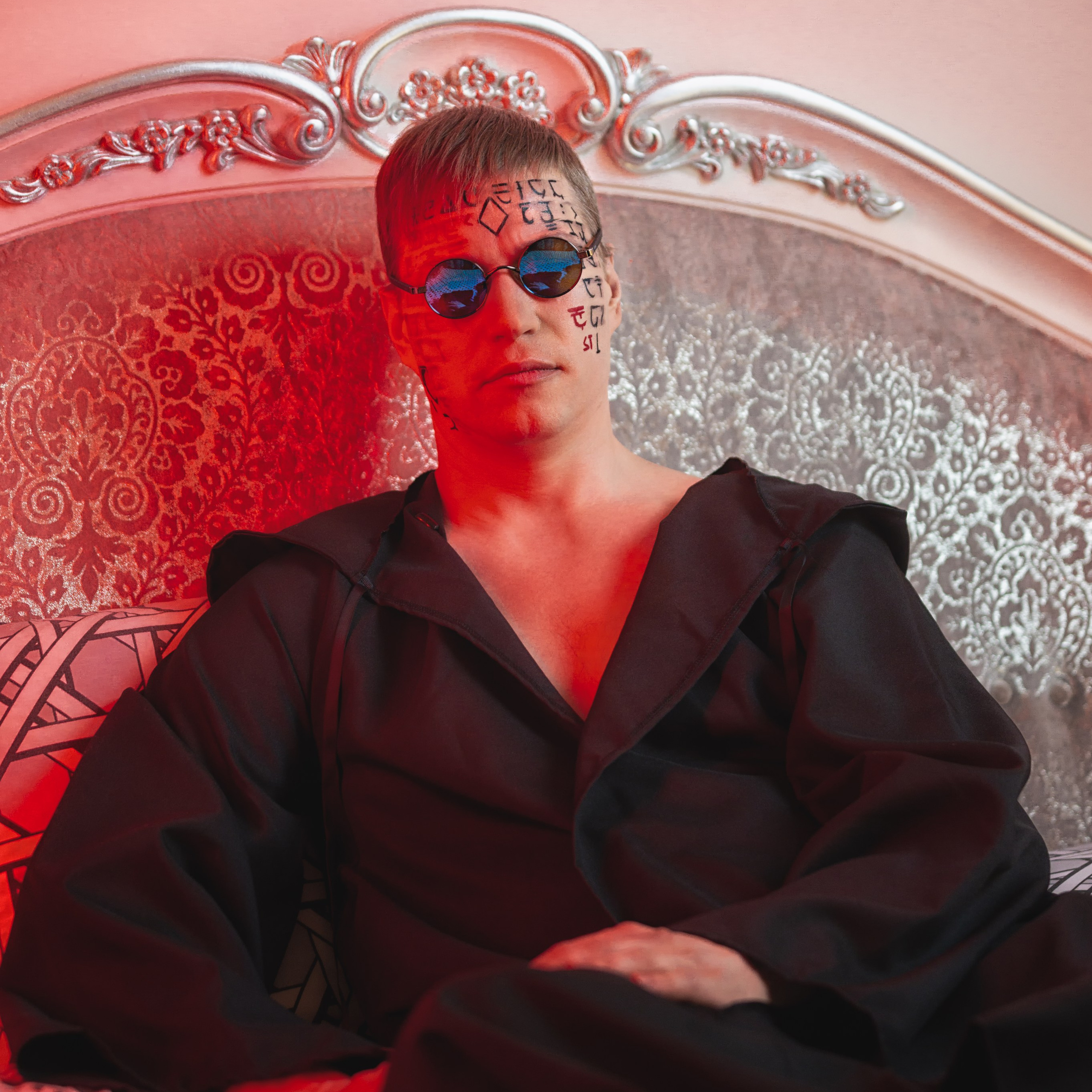 Мужчина в одежде свободного кроя и тёмных очках лежит на кровати.