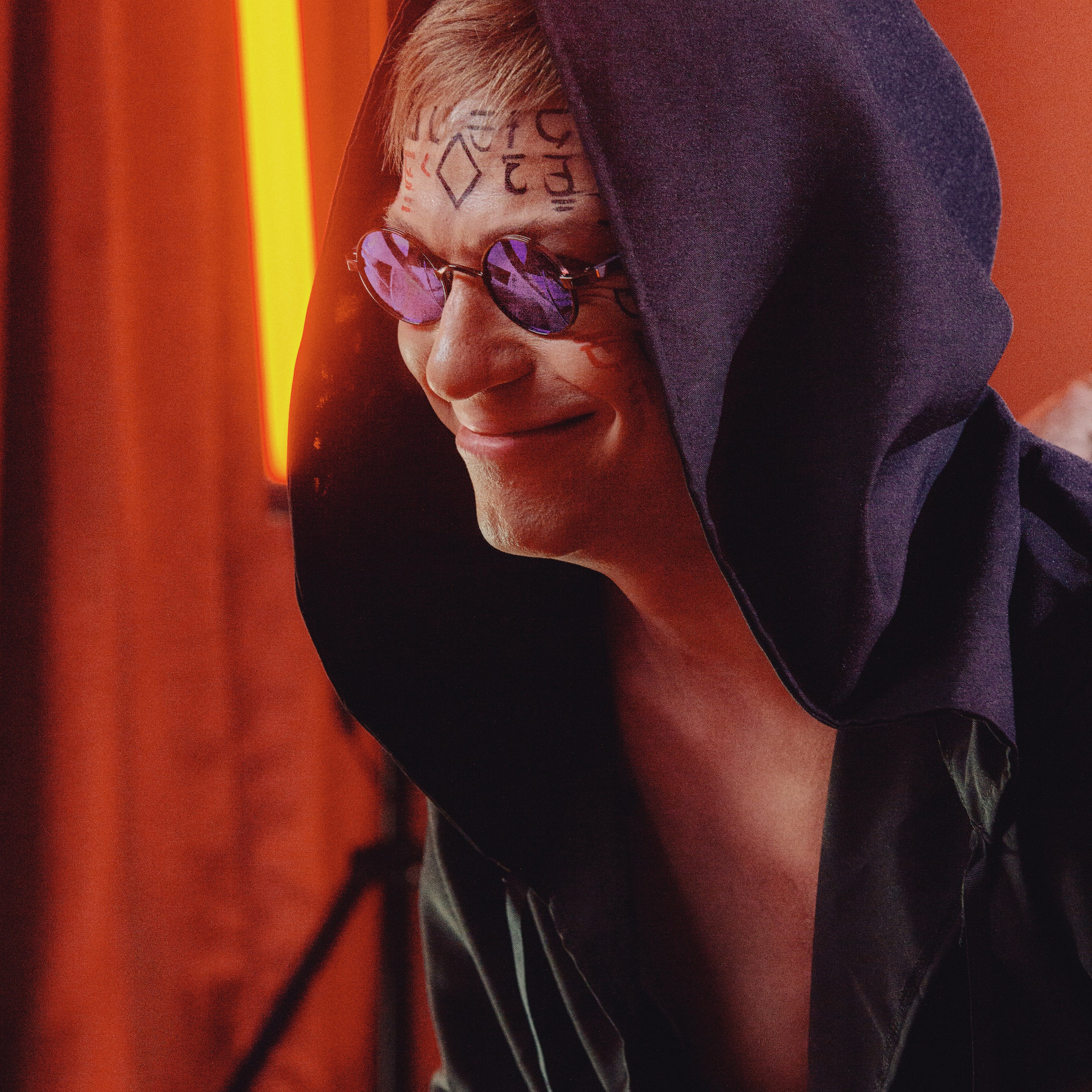 Мужчина в капюшоне и очках ехидно улыбается