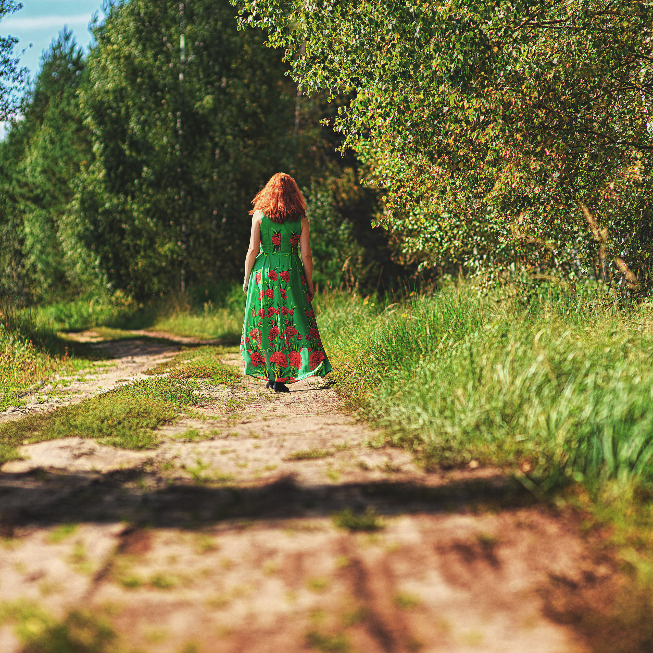 Девушка в летнем платье идет по дороге возле леса