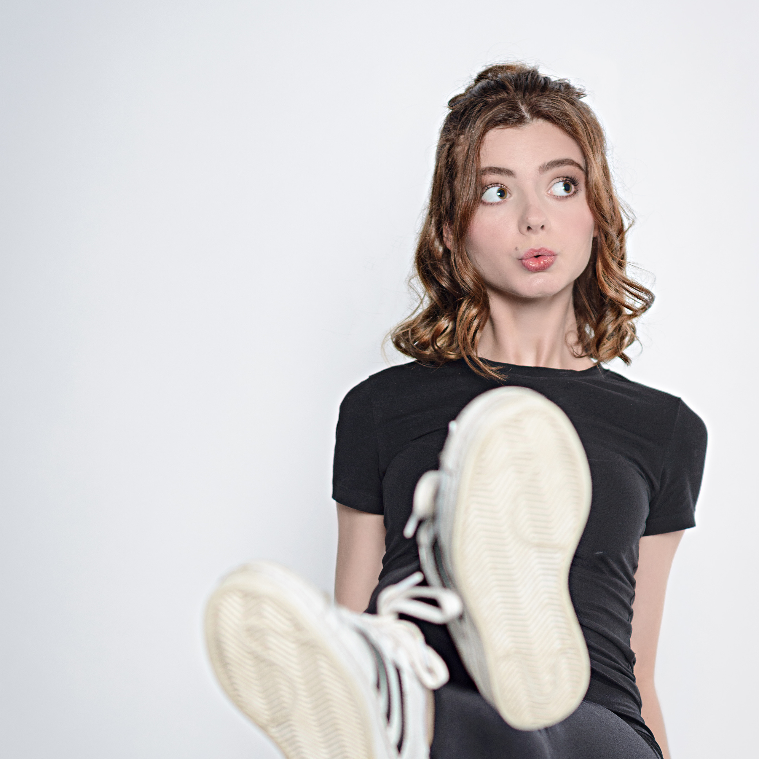 Девушка в черной одежде сидит на табуретке на белом фоне