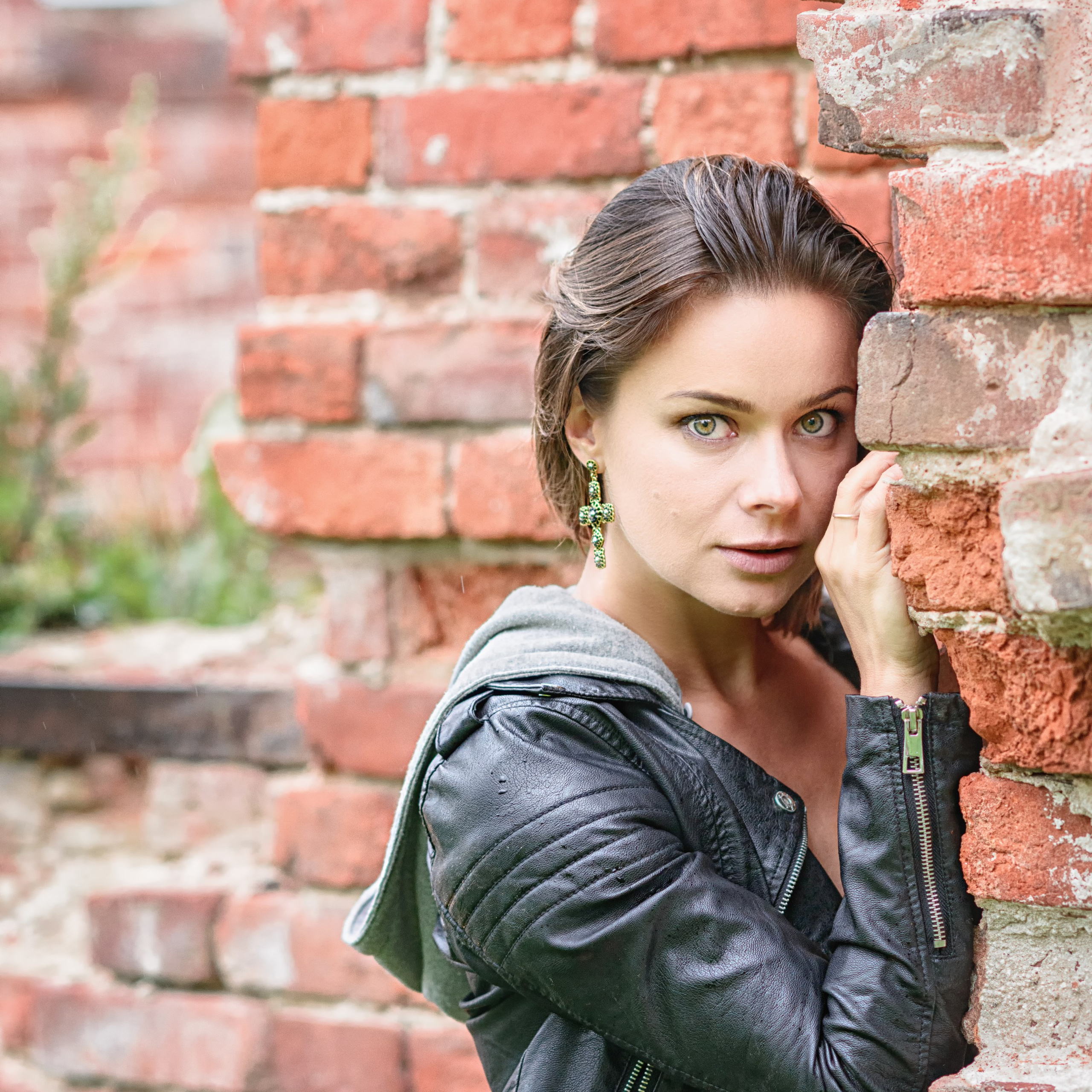 Девушка в черной кожаной куртке прижалась к стене из красного кирпича